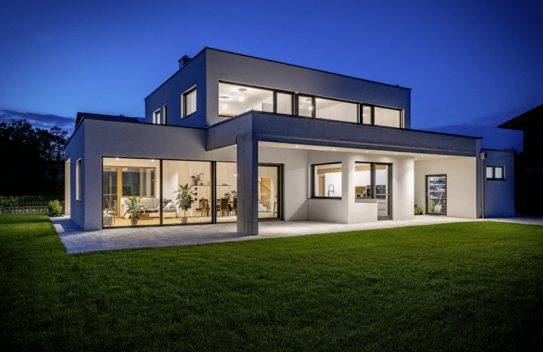 Kubische Villa mit Flachdach, Garten und überdachten Terrassenbereich bei Nacht von AL Architekt ZT.