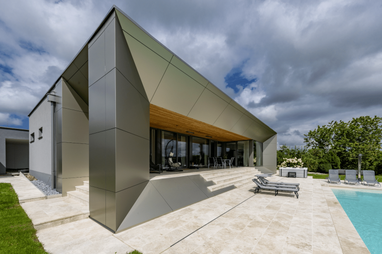 Moderne kubische Villa mit futuristischer Fassadenverkleidung in Metalloptik, großzügigem Terrassenbereich mit Steinfliesen und Pool von AL Architekt ZT.