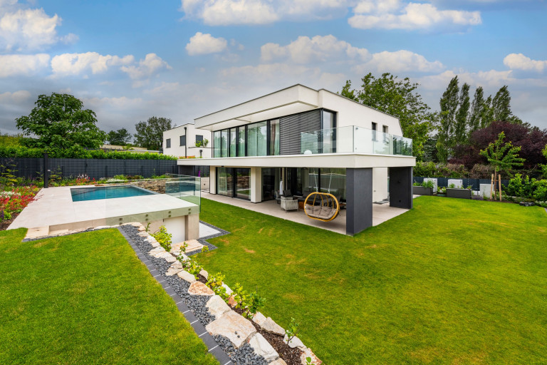 Modernes, helles Flachdach-Wohnhaus mit Glasgeländer-Balkon, großen Glasfronten, überdachter Terrasse und erhöhtem Pool von AL Architekt.