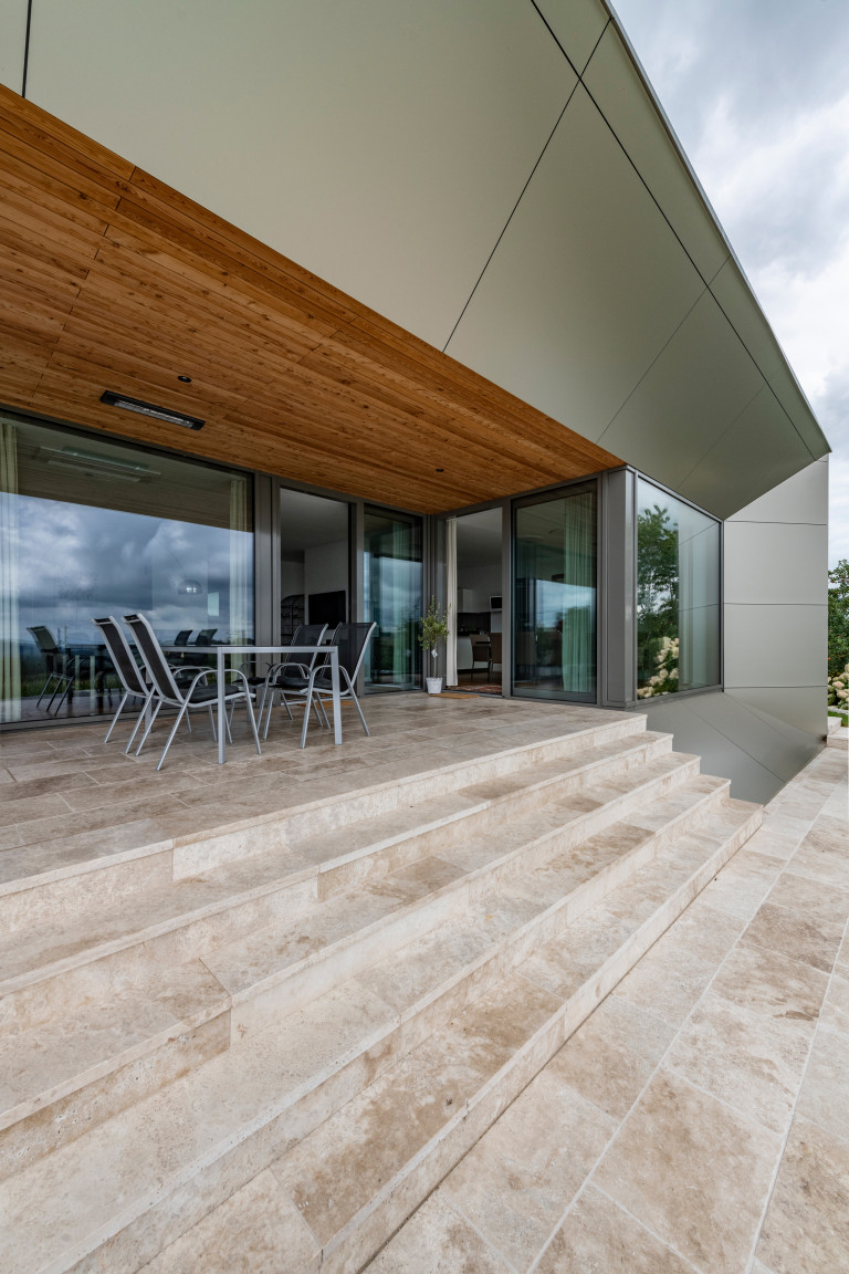 Integrierte Steinboden-Terrasse mit Holzdecke und breitem Stiegenabgang in den Garten von AL Architekt.