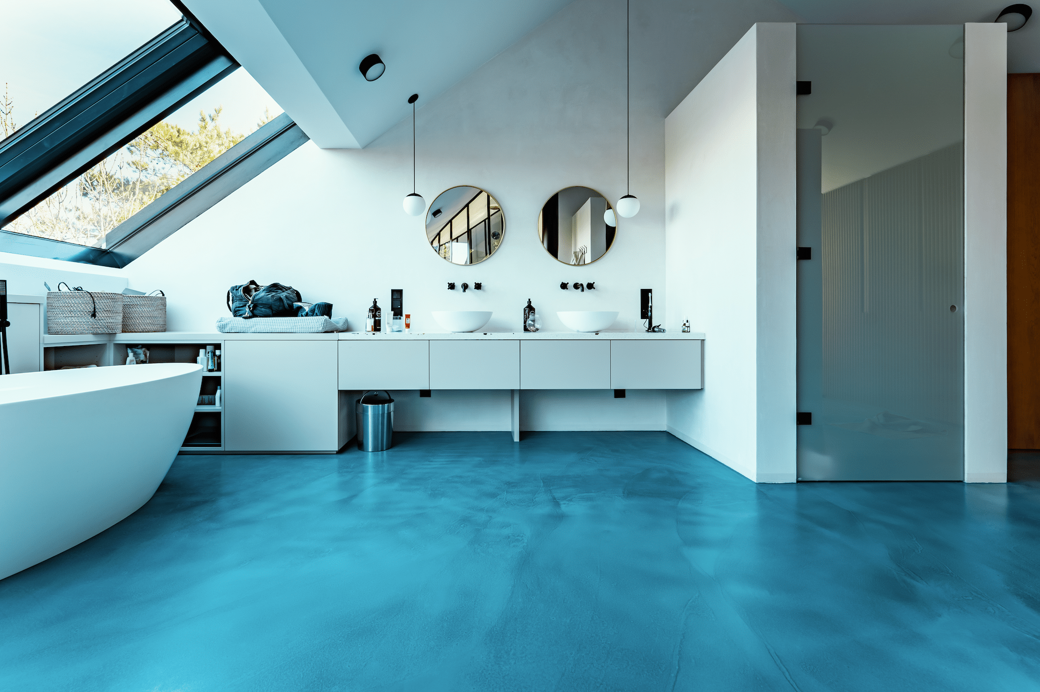 ARDEX präsentiert ein Badezimmer mit blauem Boden, einer weissen freistehenden Badewanne und einem Doppelwaschtisch mit runden Spiegeln von panDOMO.