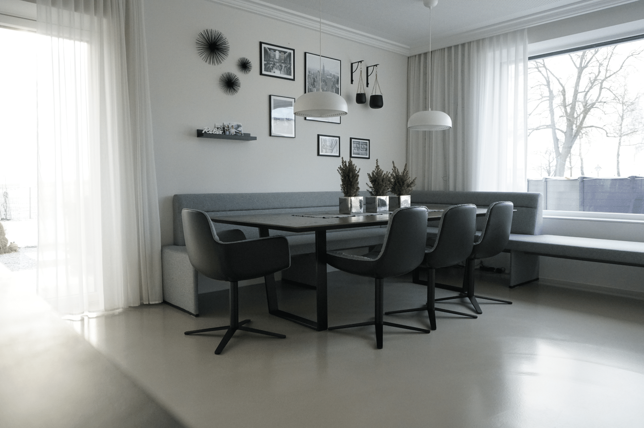 ARDEX zeigt ein Esszimmer mit dunkler Essgruppe und grauer Sitzbank mit weissen Hängelampen und hellem Boden von panDOMO.