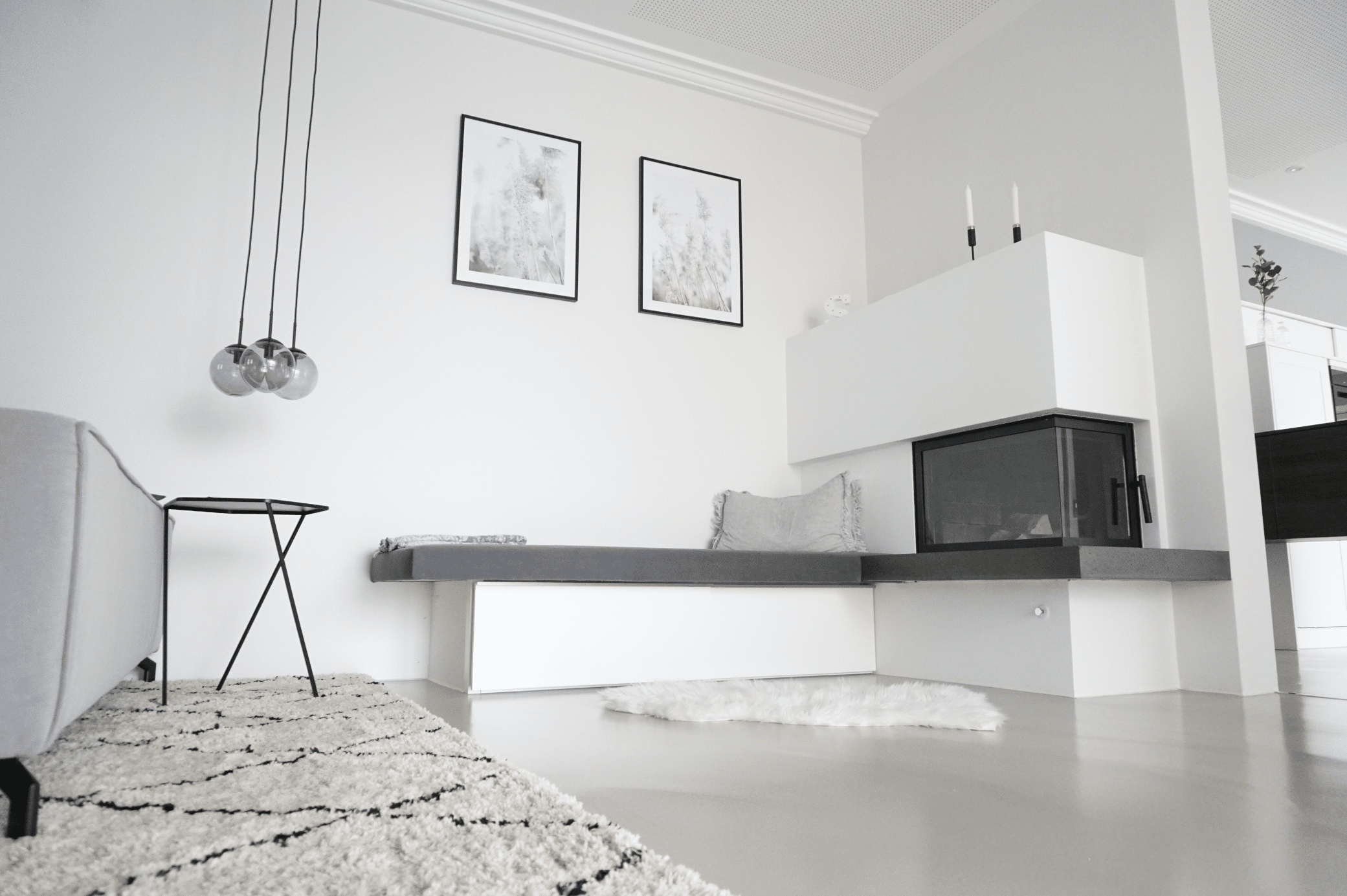 ARDEX zeigt ein Wohnzimmer mit einer hellgrauen Couch auf einem gemustertem Teppich und einem weissen Kamin mit einer Sitzbank und hellem Boden von panDOMO.