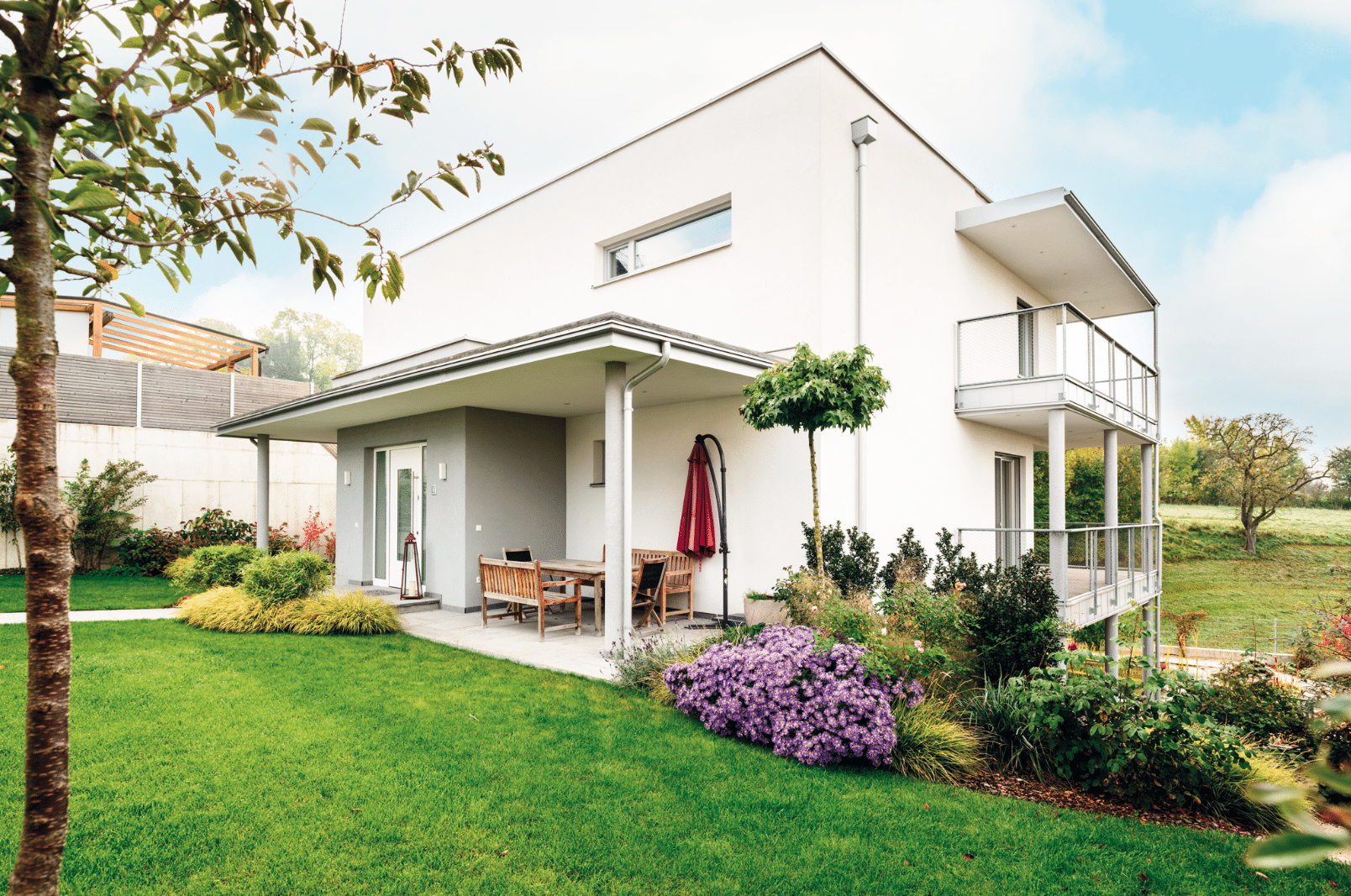 Bad Zeller zeigt ein einstöckiges Haus mit Flachdach, Balkon, Terrasse, bepflanztem Hang und Holzmöbel.