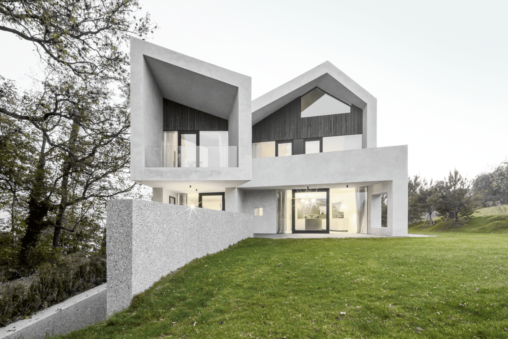 Betonmarketing Österreich zeigt ein formschönes Haus mit Betonfassade, Schrägdach, großer Fensterfront und Garten.