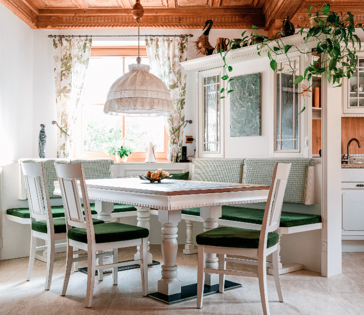 Helles Esszimmer von Böhm Möbel, gestaltet im Stil einer Bauernstube, mit Holztisch, Eckbank, Sesseln und traditionellem Lampenschirm sowie halbverbauter Vitrine als Raumteiler zur offenen Küche.
