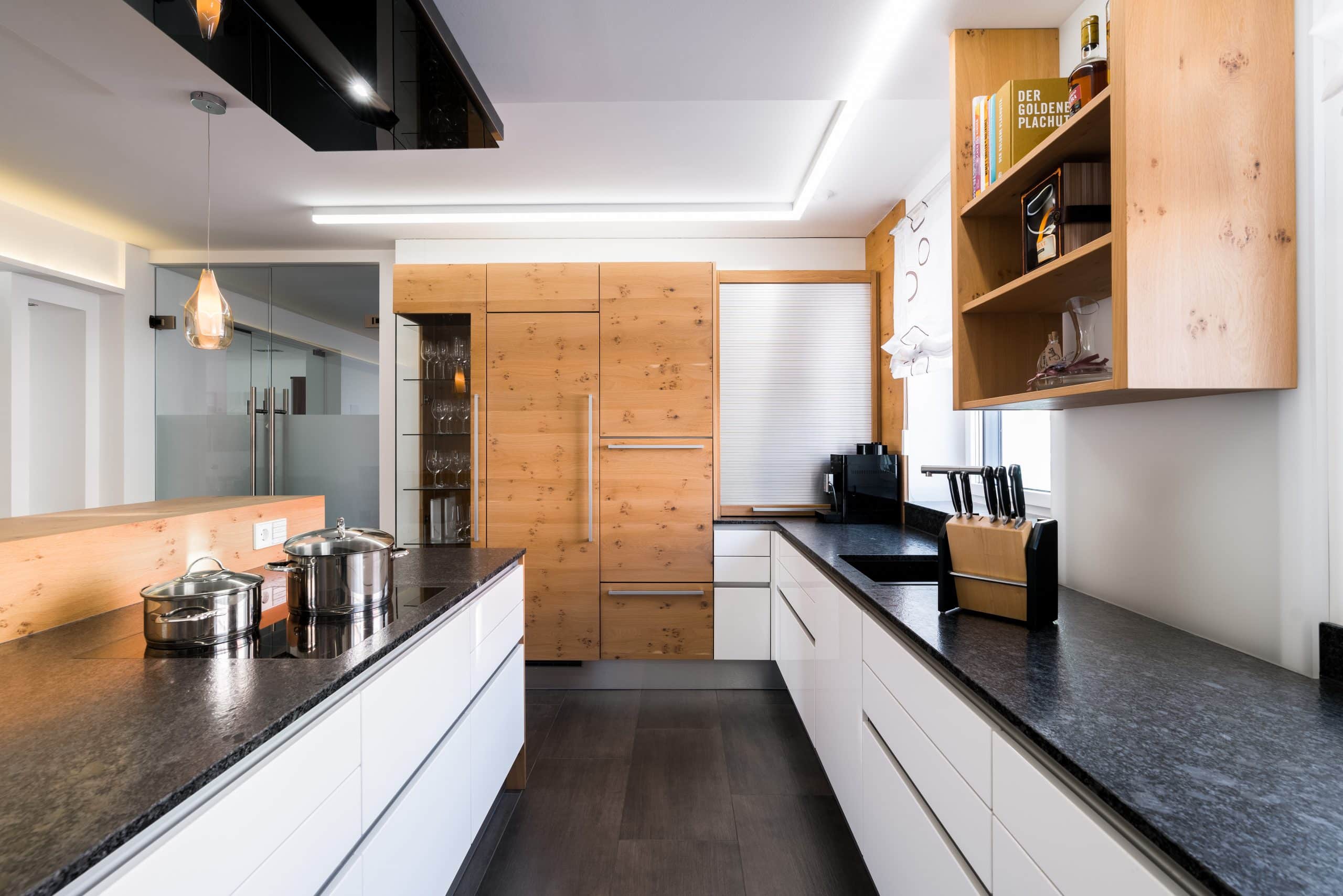 BÖHM MÖBEL zeigt eine Küche mit Schranktüren aus hellem Holz, Laden in weiß und eine dunkle Steinarbeitsplatte.