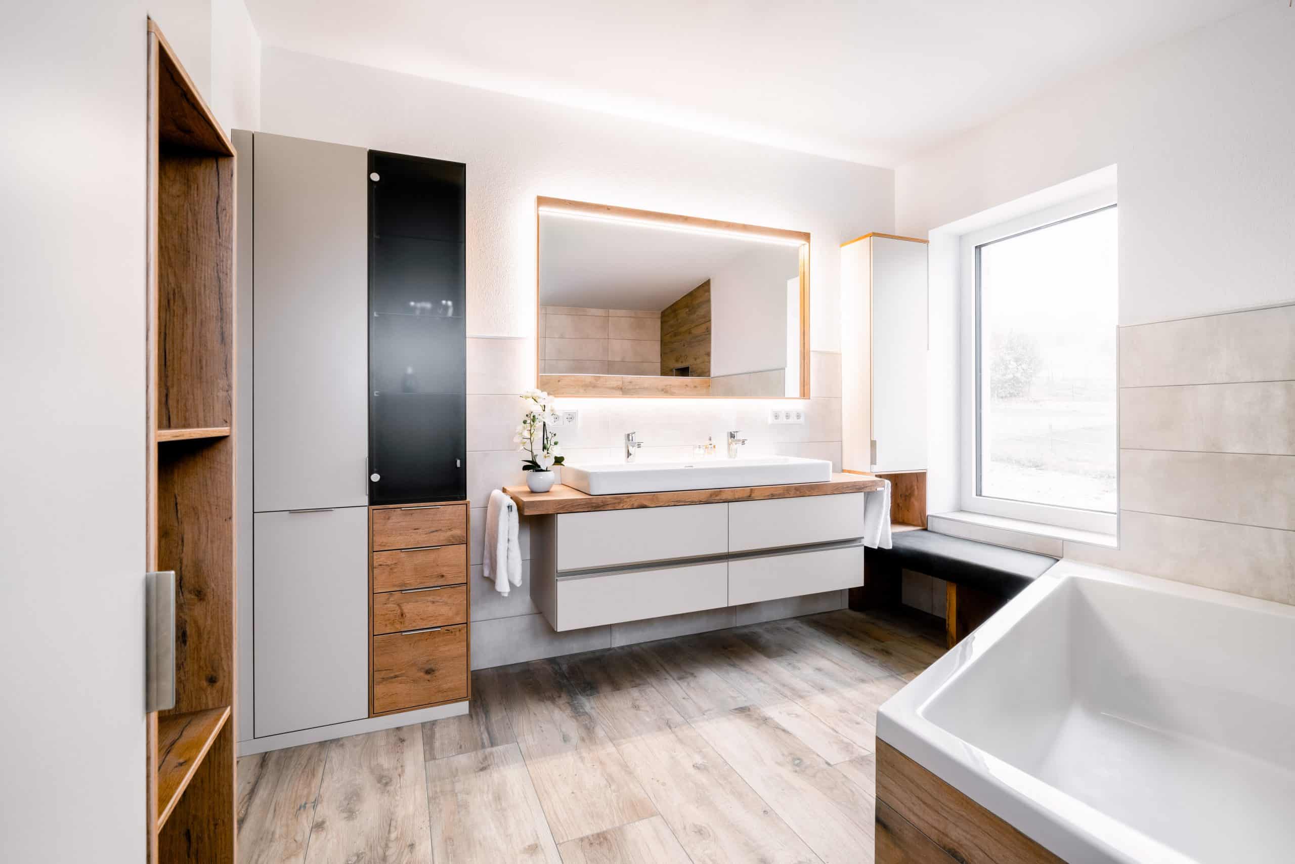 BÖHM MÖBEL zeigt ein Badezimmer in weiß mit Holzelementen, einem Doppelwaschbecken und großer Badewanne.
