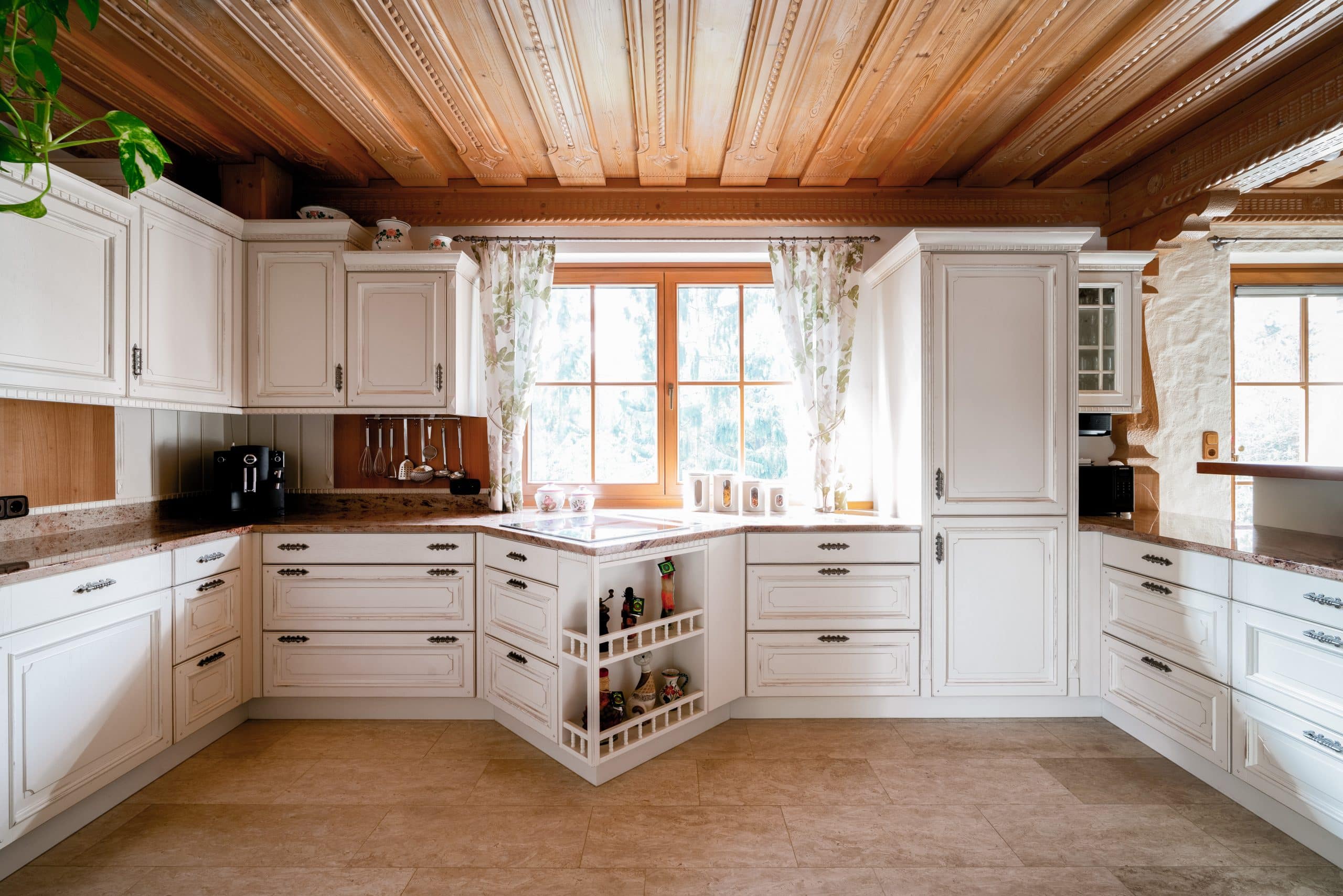 BÖHM MÖBEL zeigt eine weiße Küche im Landhausstil mit verspielten Schnitzereien und brauner Arbeitsplatte.