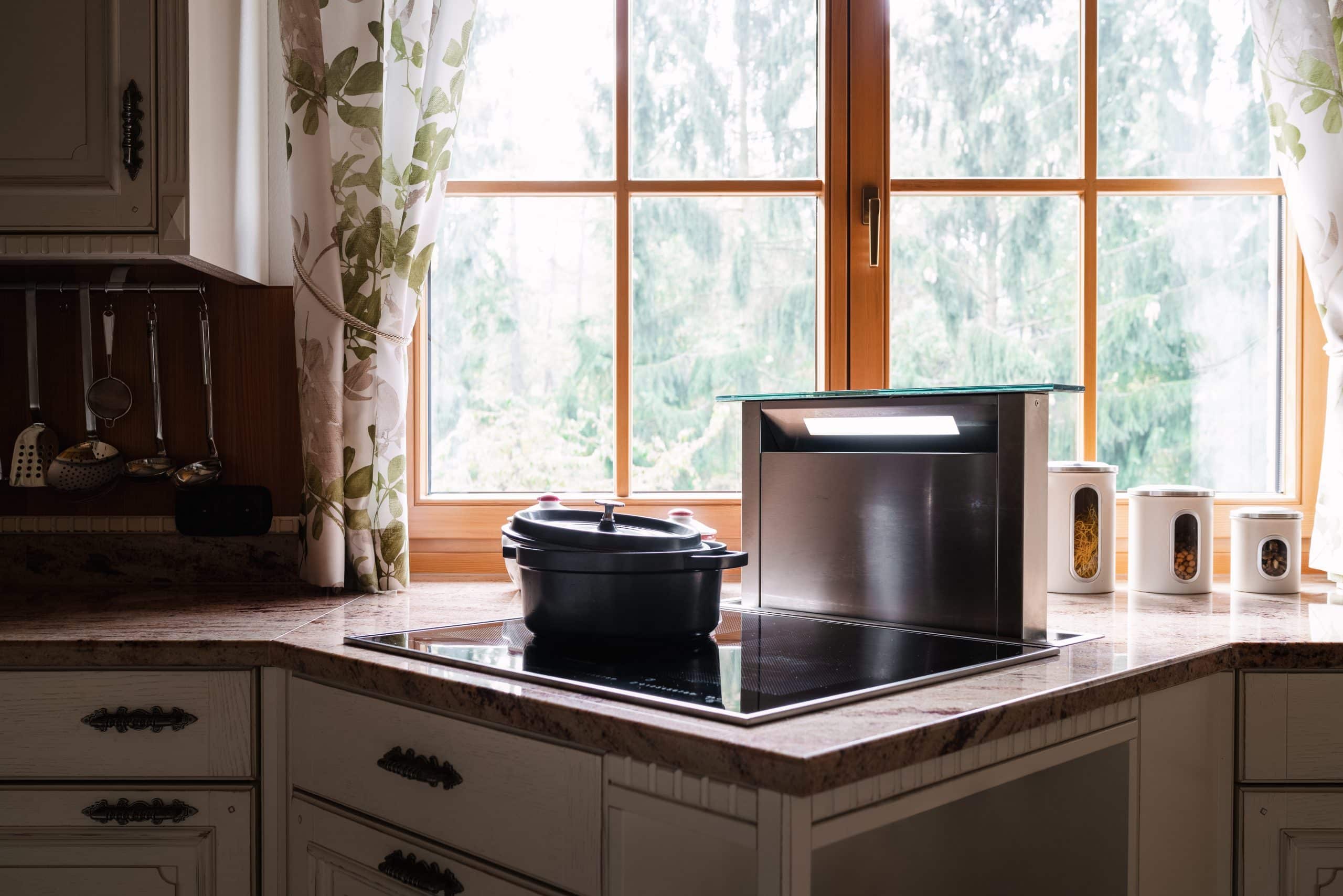 BÖHM ÖBEL zeigt eine weiße Küche im Landhausstil mit brauner Arbeitsplatte vor einem Fenster mit Holzrahmen.