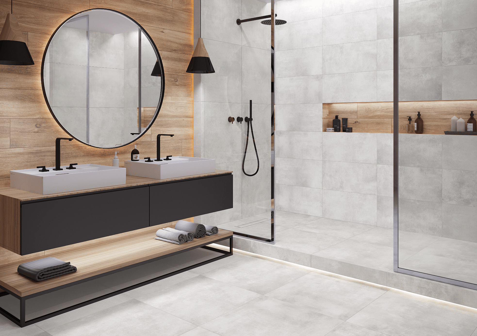 C. Bergmann zeigt ein grau gefliestes Badezimmer mit offener Dusche, zwei weissen Waschtischen und einen großen runden Spiegel von Cerrad.