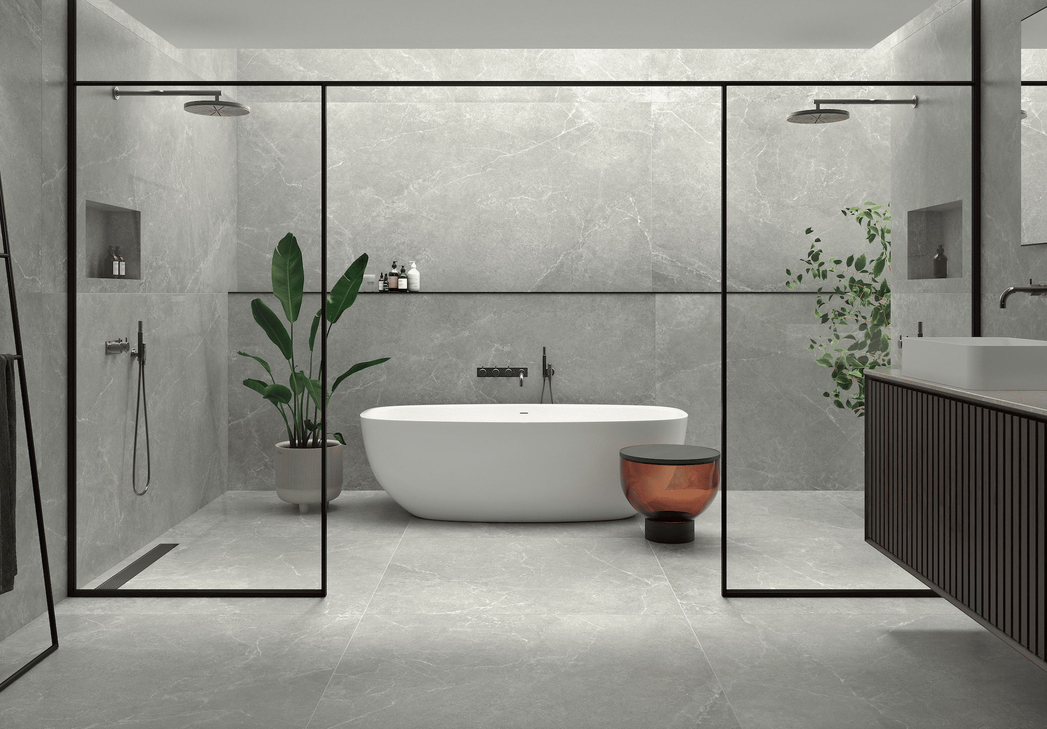C. Bergmann zeigt ein offenes Badezimmer mit grauen Wandfliesen und Fliesenboden mit freistehender Badewanne und Dusche mit Glaswand und schwarzem Rahmen von Argenta.