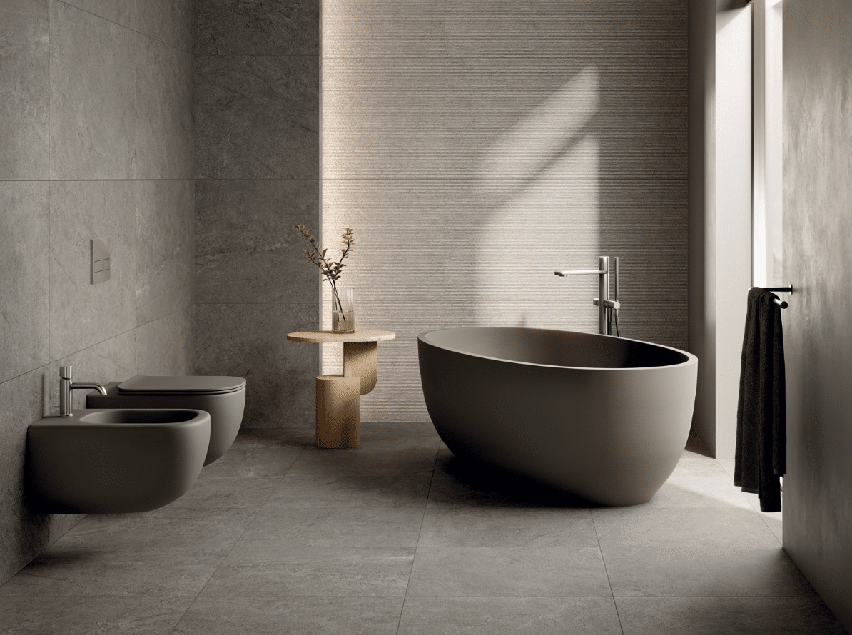 C. Bergmann zeigt ein elegantes Badezimmer mit dunklen Fliesen, einer ovalen, freistehenden Badewanne mit silberner Armatur und einer dumkelgrauen Toilette und Bidet von Abitare.