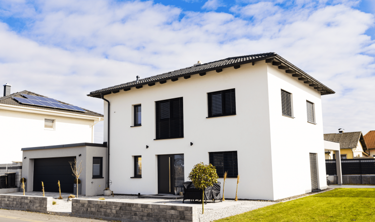 Einfamilienhaus mit Garage und überdachter Terrasse, weißer Putzfassade, schwarzen Dachziegeln und schwarzen Alufenstern von DIALOG Haus.