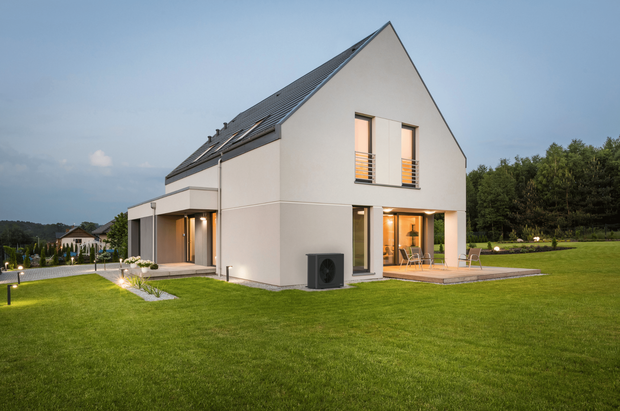 Dimplex zeigt ein helles Einfamilienhaus, mit großen Fenstern, einem gepflegtem Garten und gefliester Terrasse mit einer Essgruppe und einer schwarzen Wärmepumpe die außen angebracht ist.