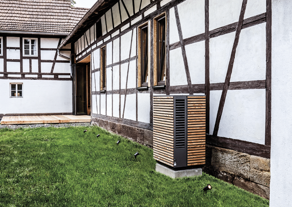 Dimplex zeigt eine Wärmepumpe mit Holzverkleidung im Außenbereich eines älteren Landhauses.