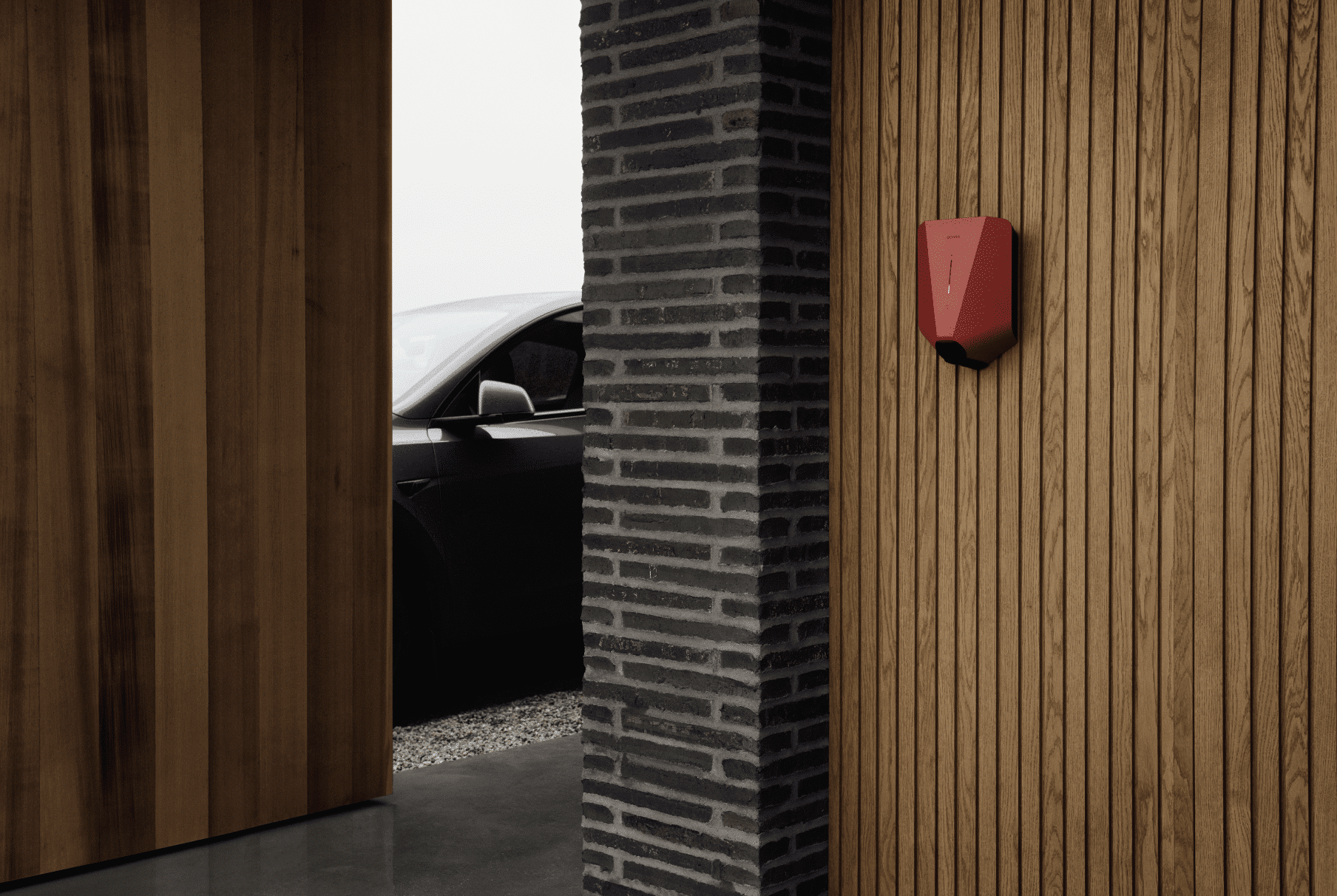 Eine rote Wallbox zum Aufladen von Elektroautos von easee, montiert an einem modernen Holzhaus.