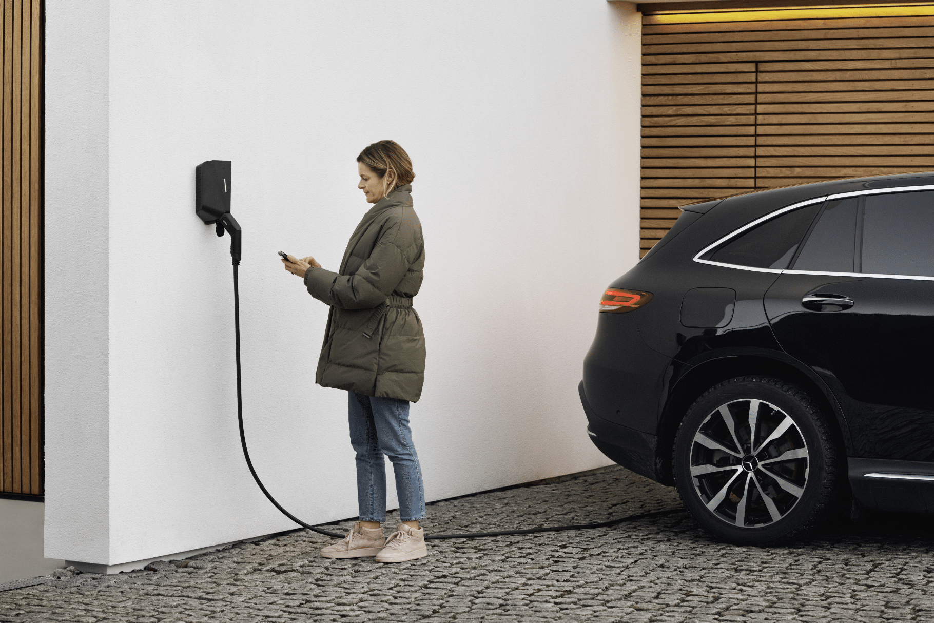 easee zeigt eine Frau, die ihr Elektroauto zu Hause mit einer schwarzen Wallbox auflädt.