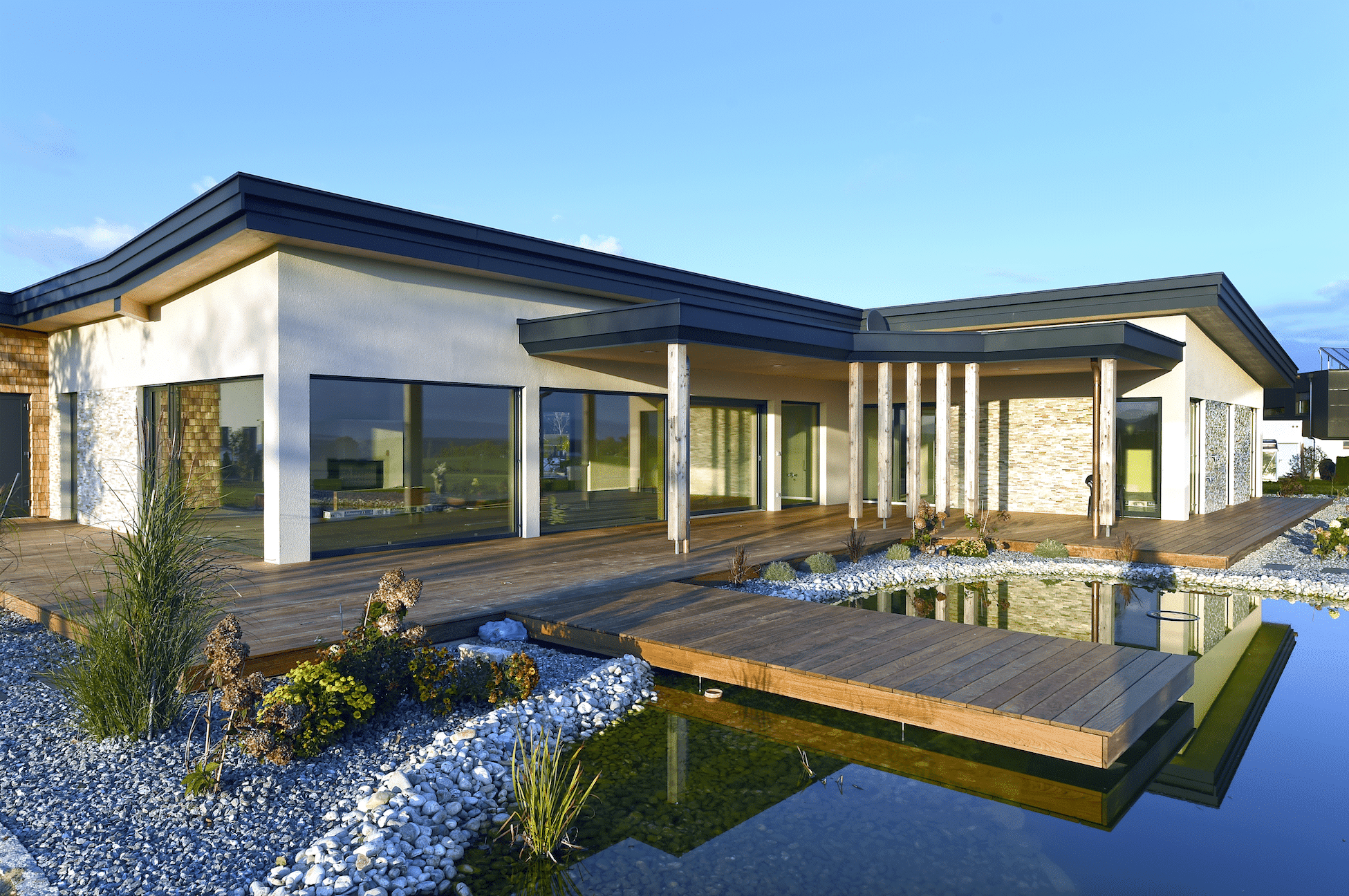 Außenaufnahme eines Einfamilienhauses mit Holzterrasse, Holzsteg und Schwimmteich der Firma Erler Haus.