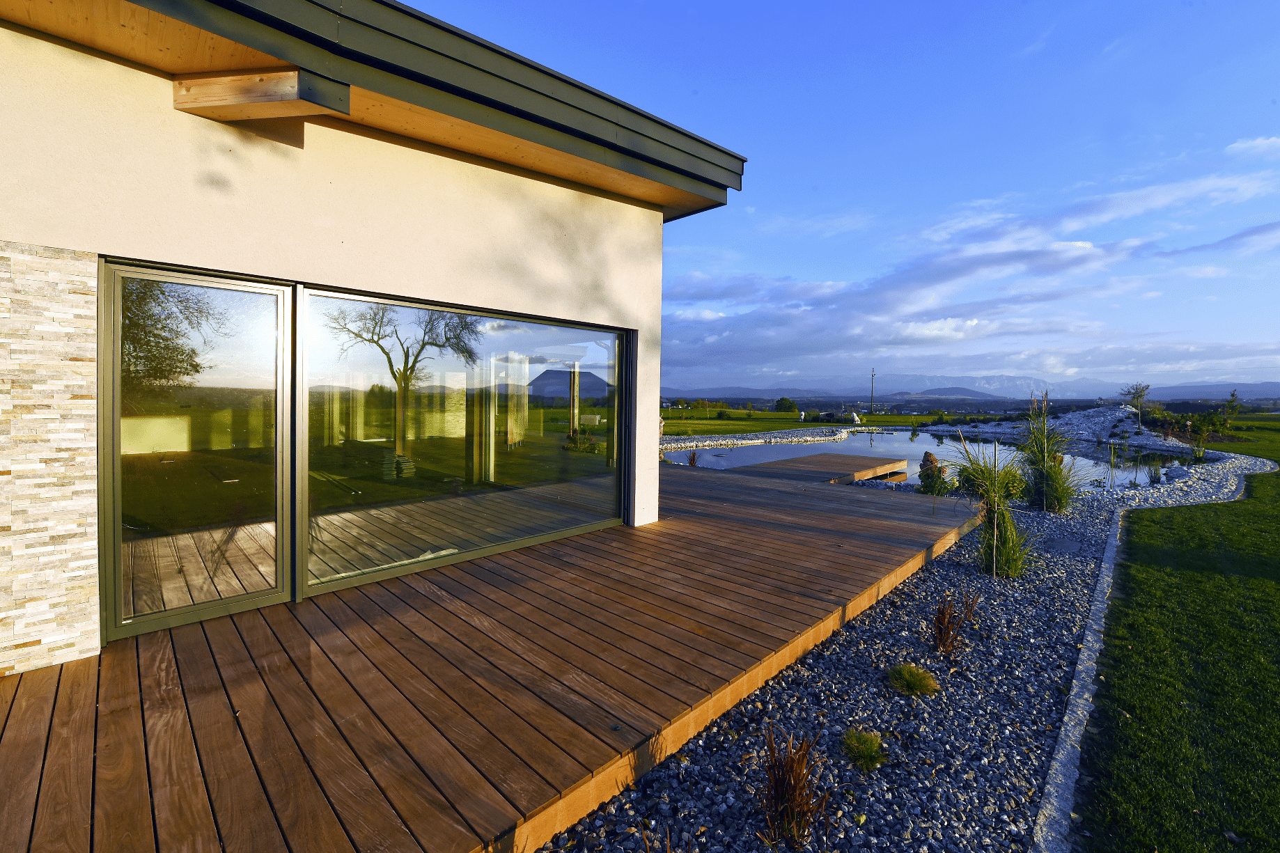 Gezoomte Außenaufnahme eines Einfamilienhauses mit Holzterrasse und Schwimmteich der Firma Erler Haus.