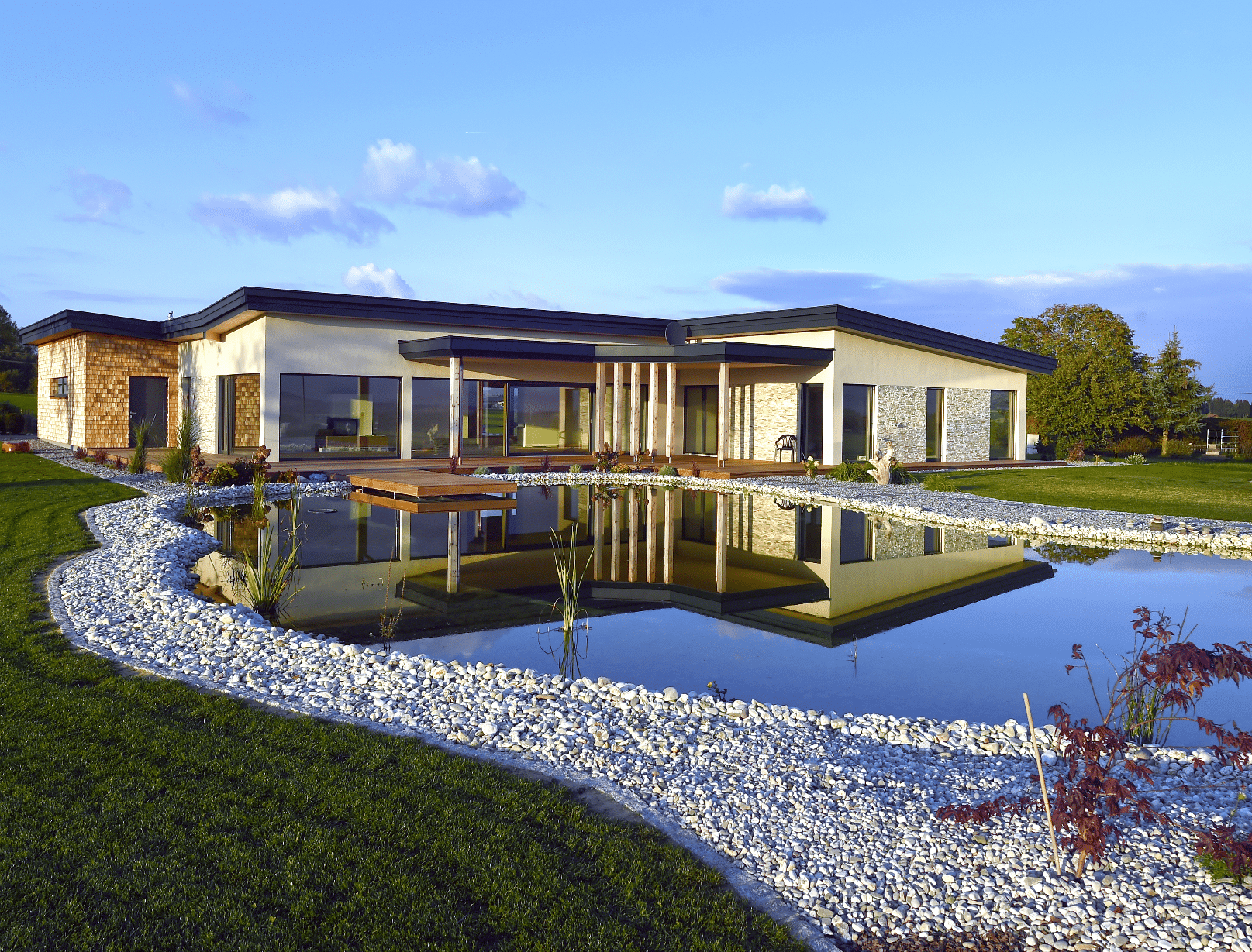 Außenaufnahme eines Einfamilienhauses mit Garten bestehend aus Holzterrasse, Holzsteg und Schwimmteich der Firma Erler Haus.
