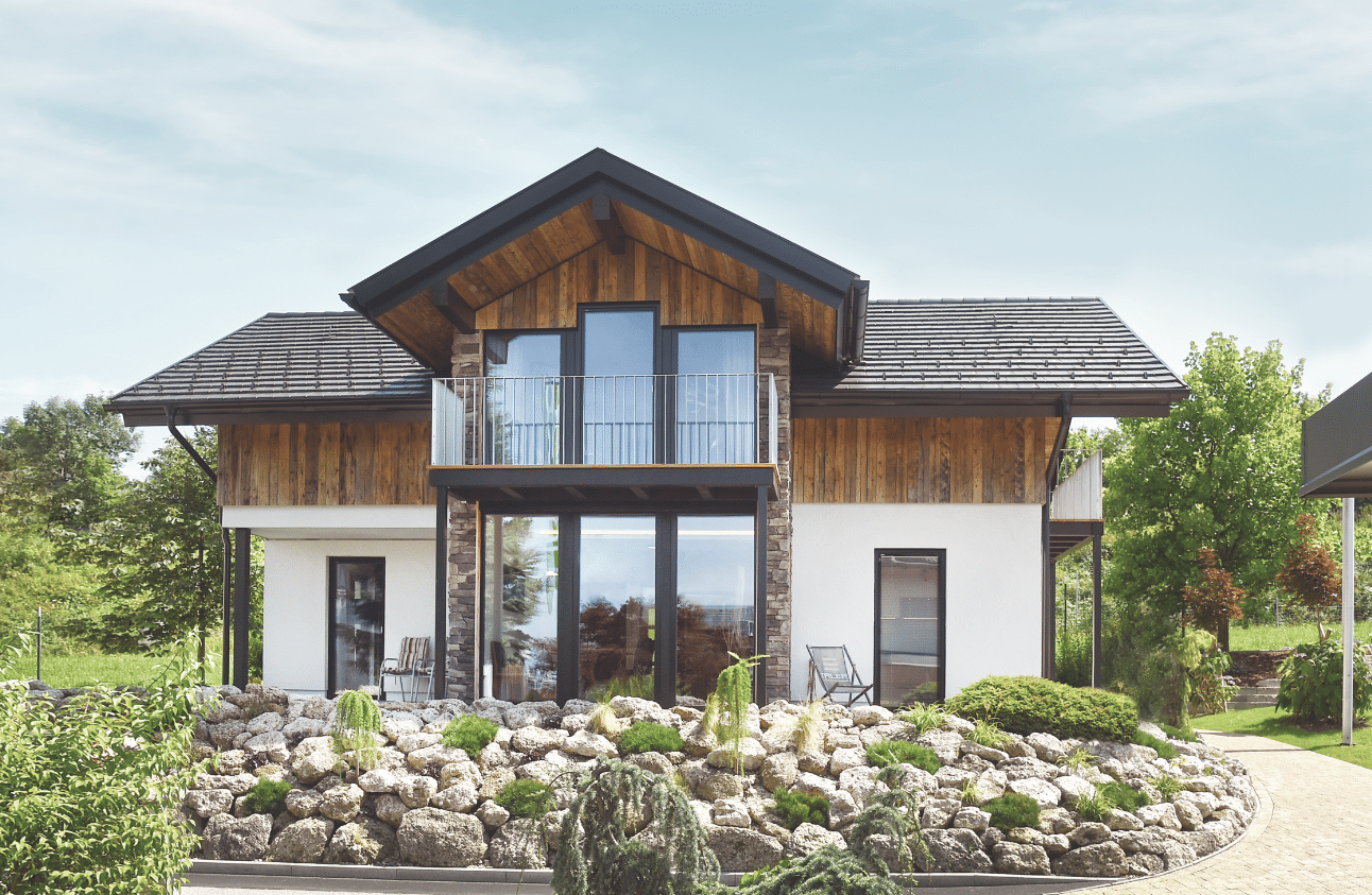 Ein schönes Einfamilienhaus mit Holzelementen und großem, überdachten Balkon mit Metallgeländer und einer Terrasse von ERLER BAU GmbH.