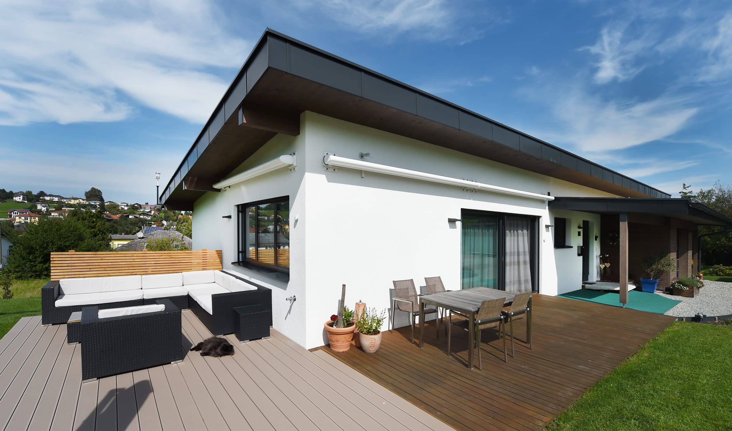 Ein modernes weisses Haus mit Flachdach und einer Terrasse mit einer Sitzgruppe und gemütlicher Sitzlounge auf Holzboden von ERLER BAU GmbH.