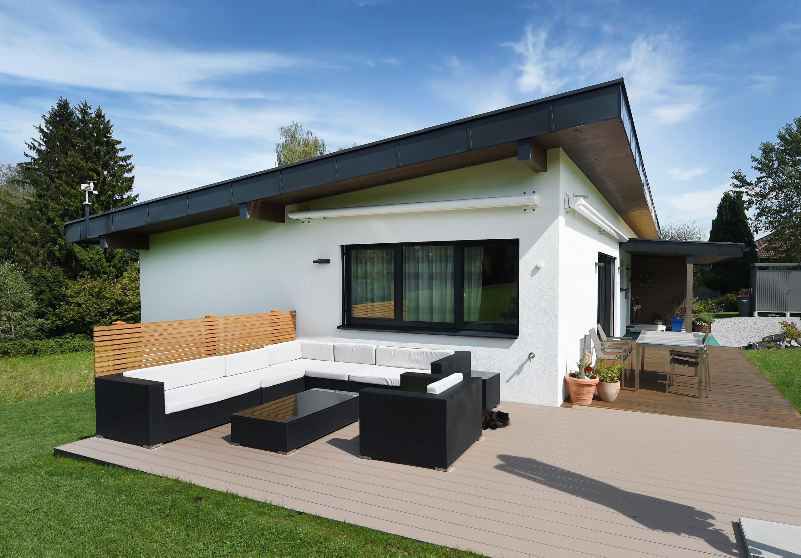 Ein modernes weisses Haus mit Flachdach und Terrasse mit gemütlicher Sitzlounge auf Holzboden von ERLER BAU GmbH.