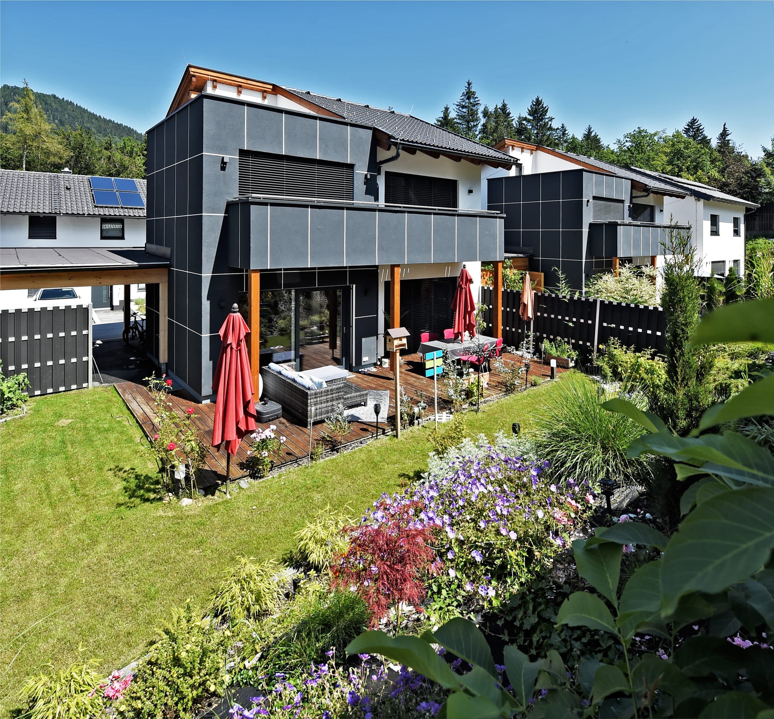 ERLER BAU GmbH zeigt ein Einfamilienhaus mit großer Terrasse mit Holzboden und gemütlichen Sitzmöbeln und gepflegtem Rasen.