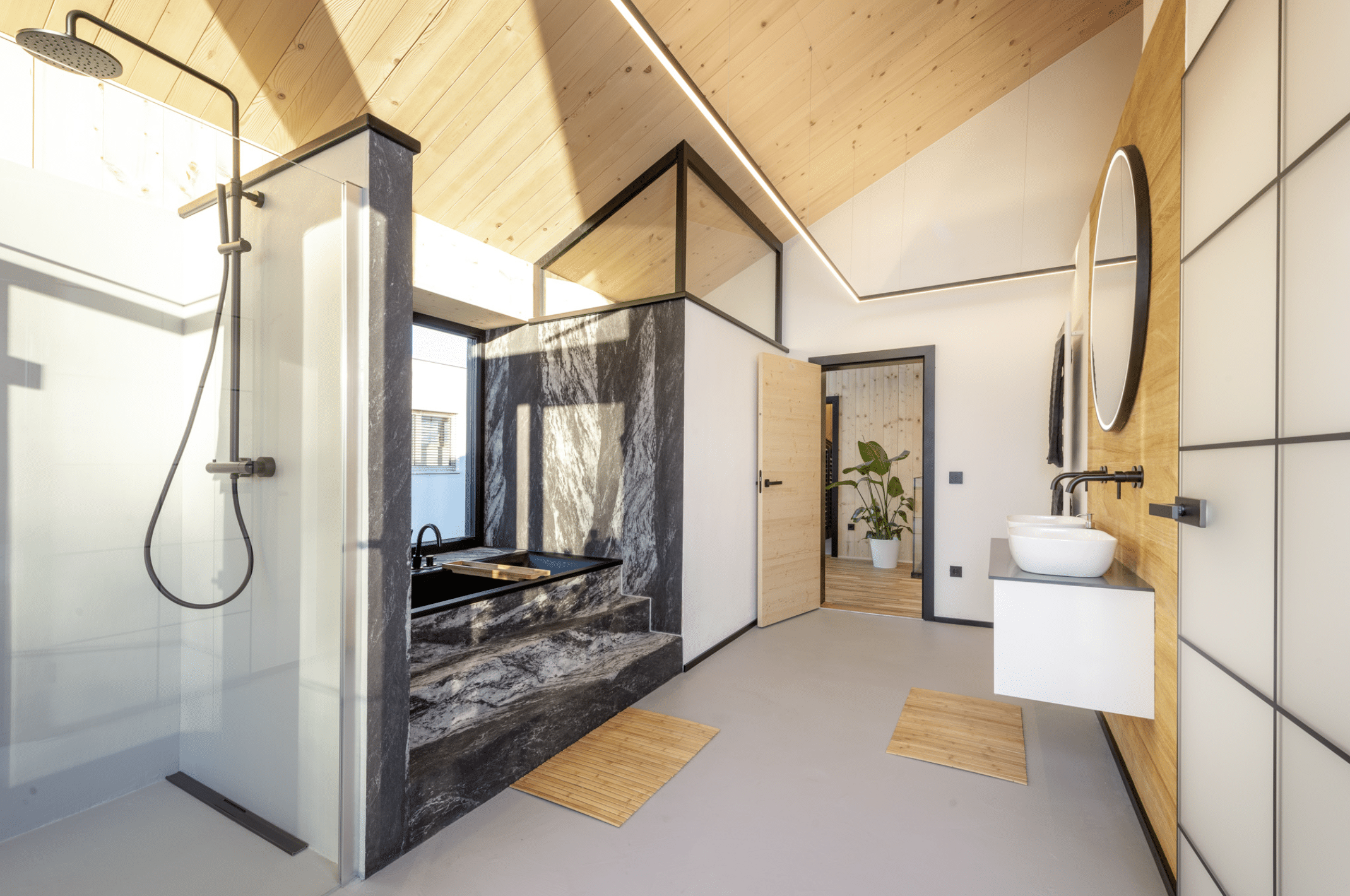 Erler Haus zeigt das sehr helle Badezimmer eines Holzriegelhauses mit moderner Einrichtung, marmorierter Badewanne und großen Terrassentüren.