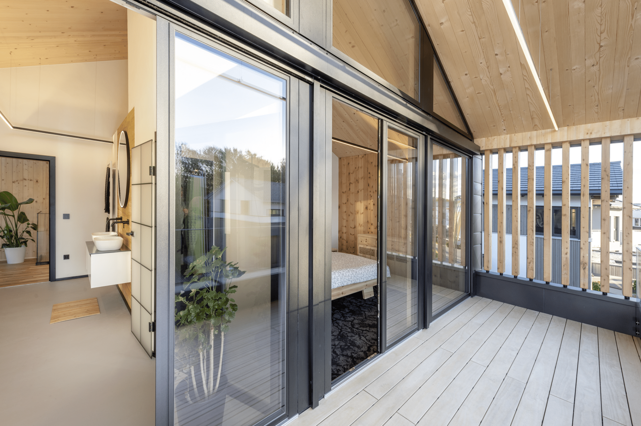 Erler Haus zeigt den Balkon eines Holzriegelhauses, welcher durch große Glas-Schiebetüren in Bade- und Schlafzimmer führt.