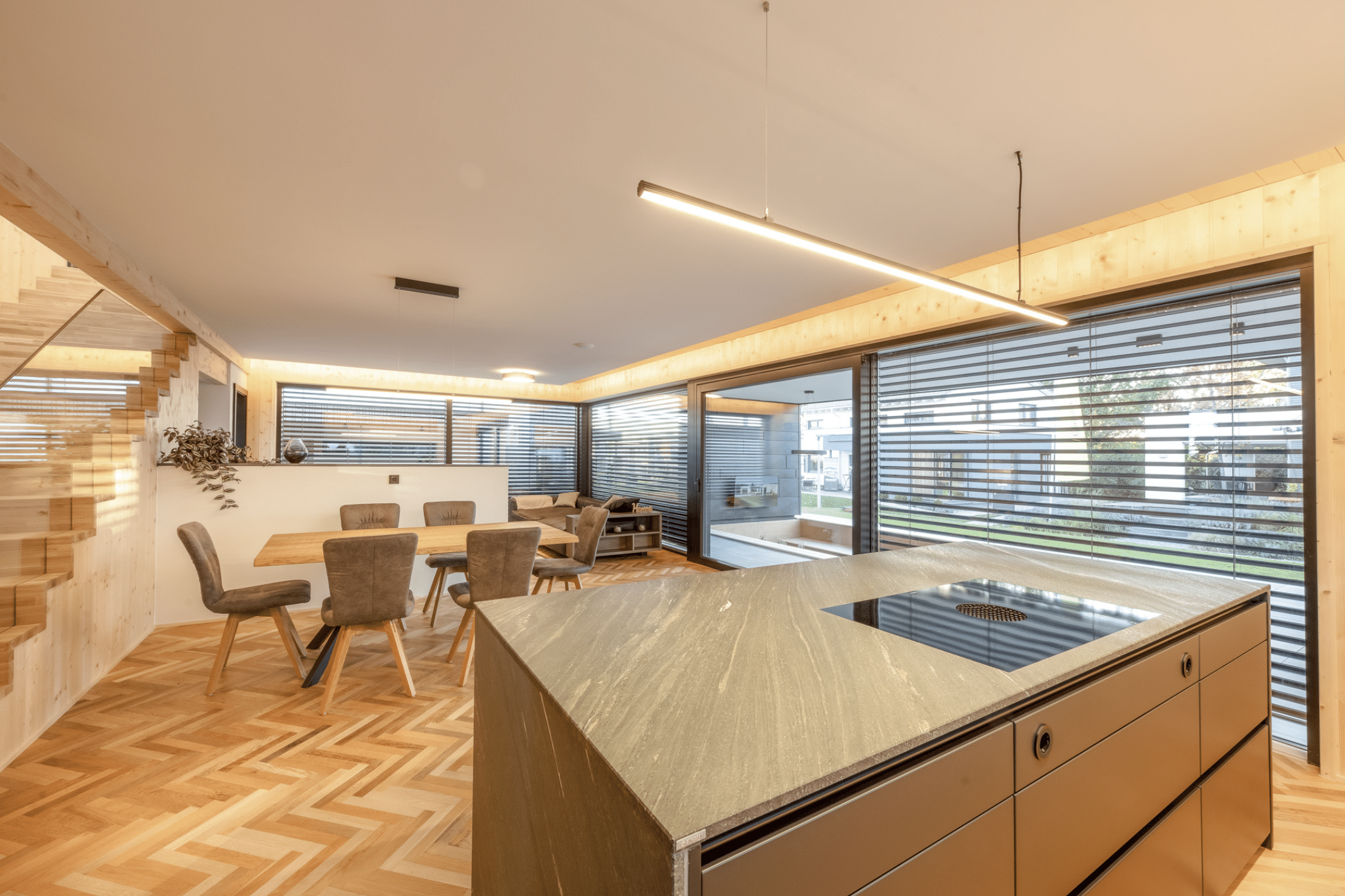 Erler Haus zeigt den modernen Essbereich eines Holzriegelhauses inklusive Küche mit marmorierter Arbeitsplatte und Fischgrätboden.