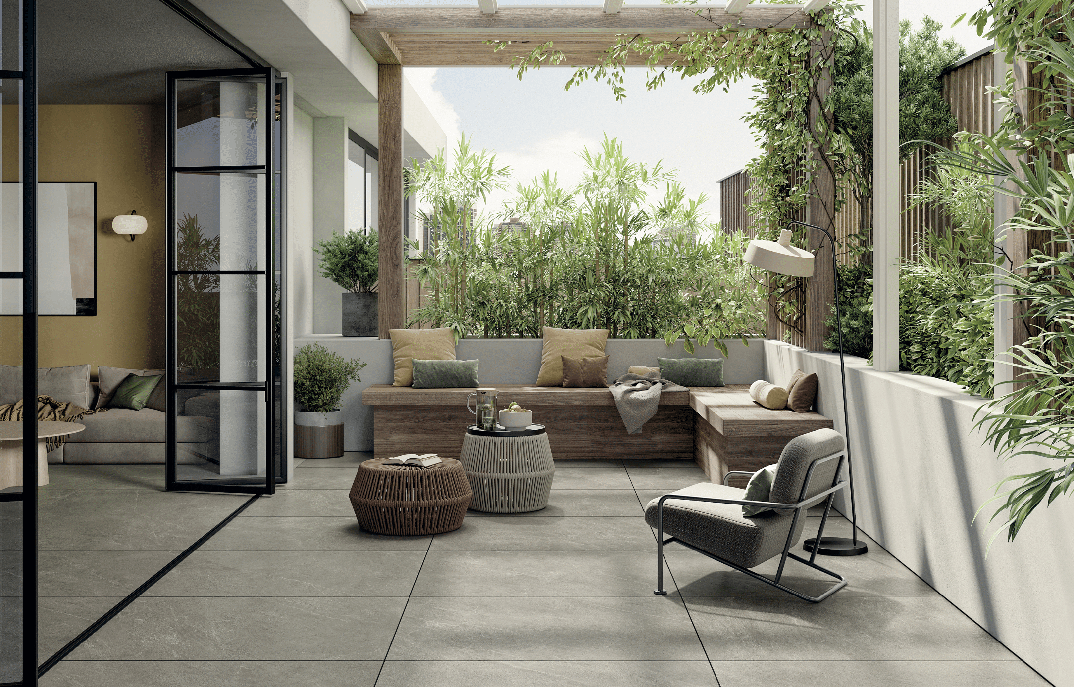 Felbermair zeigt eine überdachte Terrasse mit grauem Fliesenboden und gemütlicher Sitzbank aus Holz mit vielen Kissen und einer Glasfalttüre mit schwarzem Rahmen als Zugang zum Wohnzimmer von Mirage.