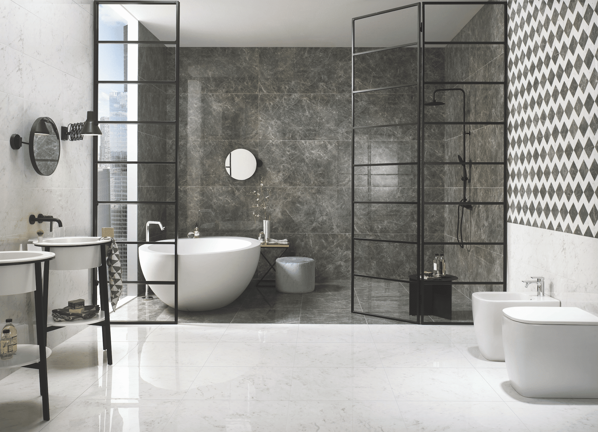 Helles, gefliestes Badezimmer mit Walkin-Dusche und freistehender Badewanne hinter einer Glaswand sowie Toiletten und Waschbecken vor dunkelgrauen Muster-Wandfliesen der Firma Fliesendorf.