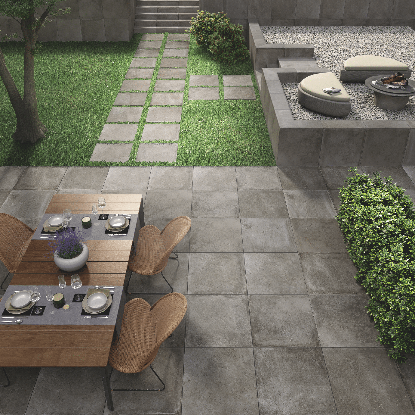 Fliesendorf zeigt einen Garten mit gefliester Terrasse, einem Holztisch, Rattanstühlen und Zugang aus großen Natursteinplatten mit Stufen zu einem Loungebereich.