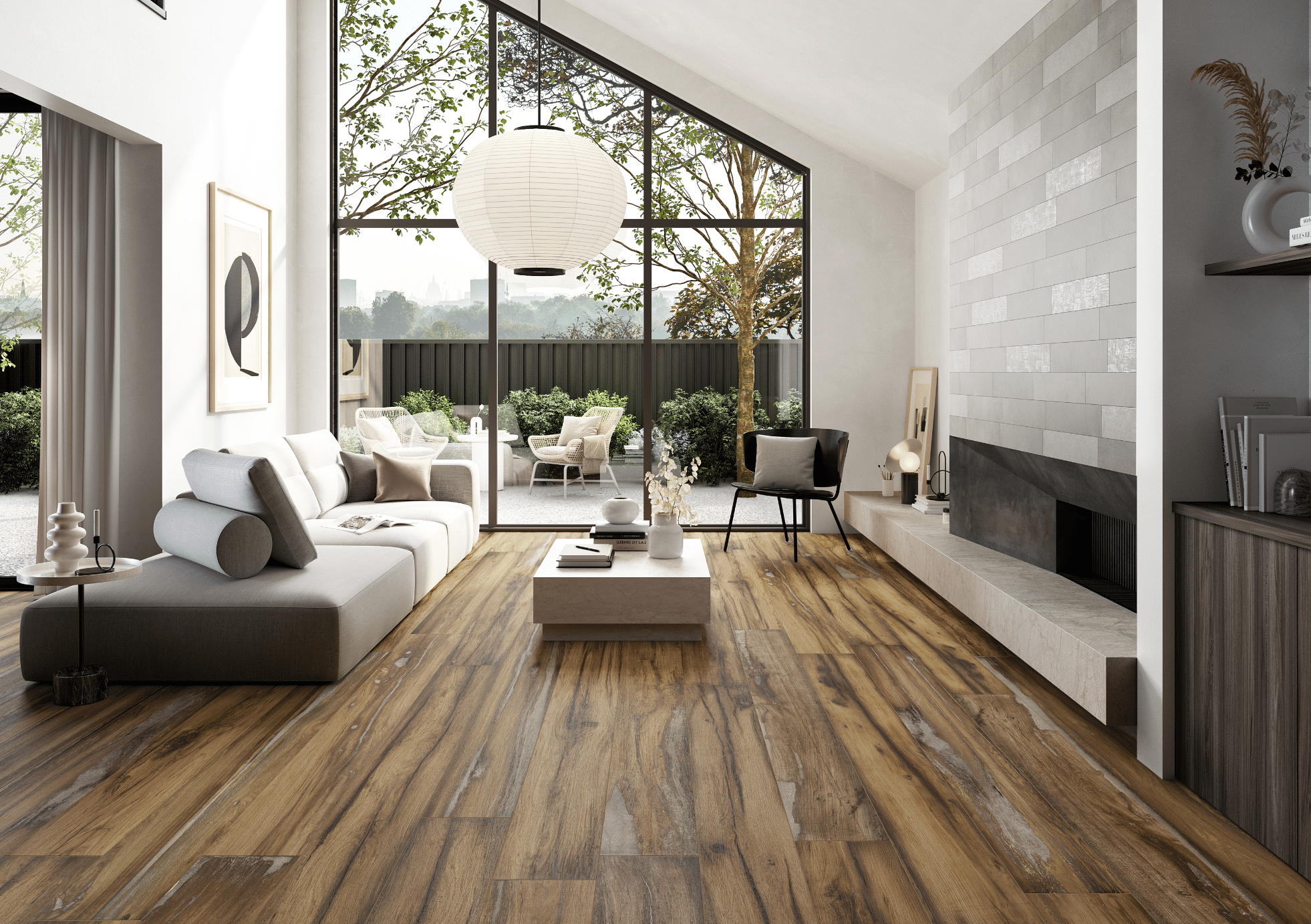 Fliesendorf zeigt ein Wohnzimmer mit Holzboden, heller Couch, runder Pendelleuchte und großer Glasfront mit Blick auf die geflieste Terrasse mit hellen Möbeln.