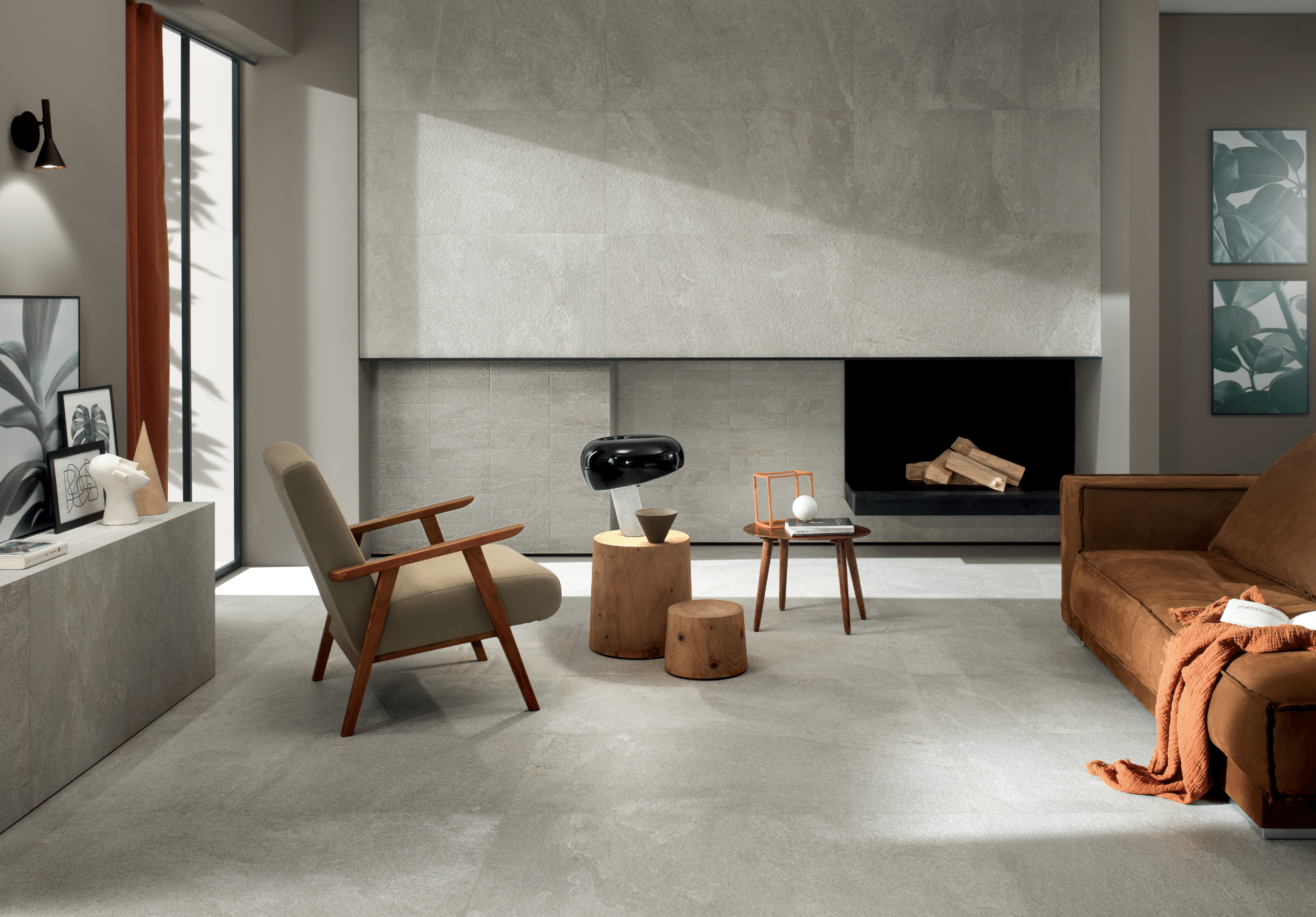 Fliesendorf zeigt ein Wohnzimmer mit gefliesten Boden in grau und einem braunen Sofa, einem Loungestuhl und einem Beistelltisch aus Holz vor einem in der Wand verbauten Kamin.