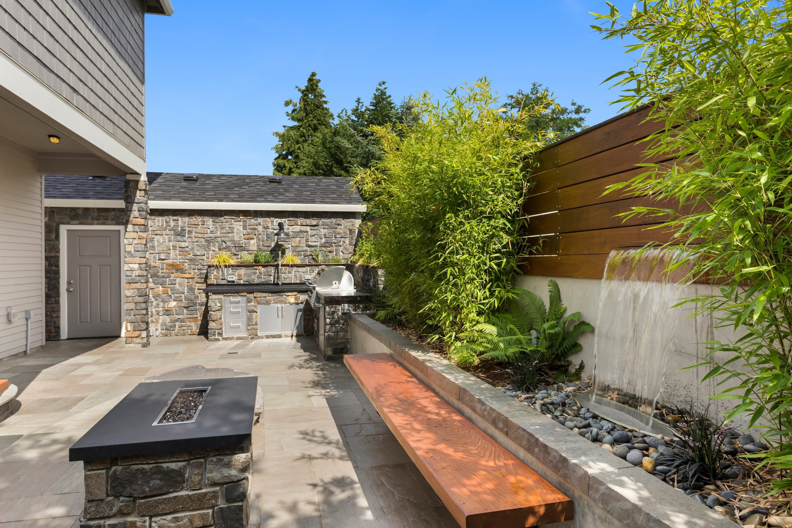 Terrasse mit praktischer Outdoorküche, gemütlicher Feuerstelle und einladendem Wasserspiel.