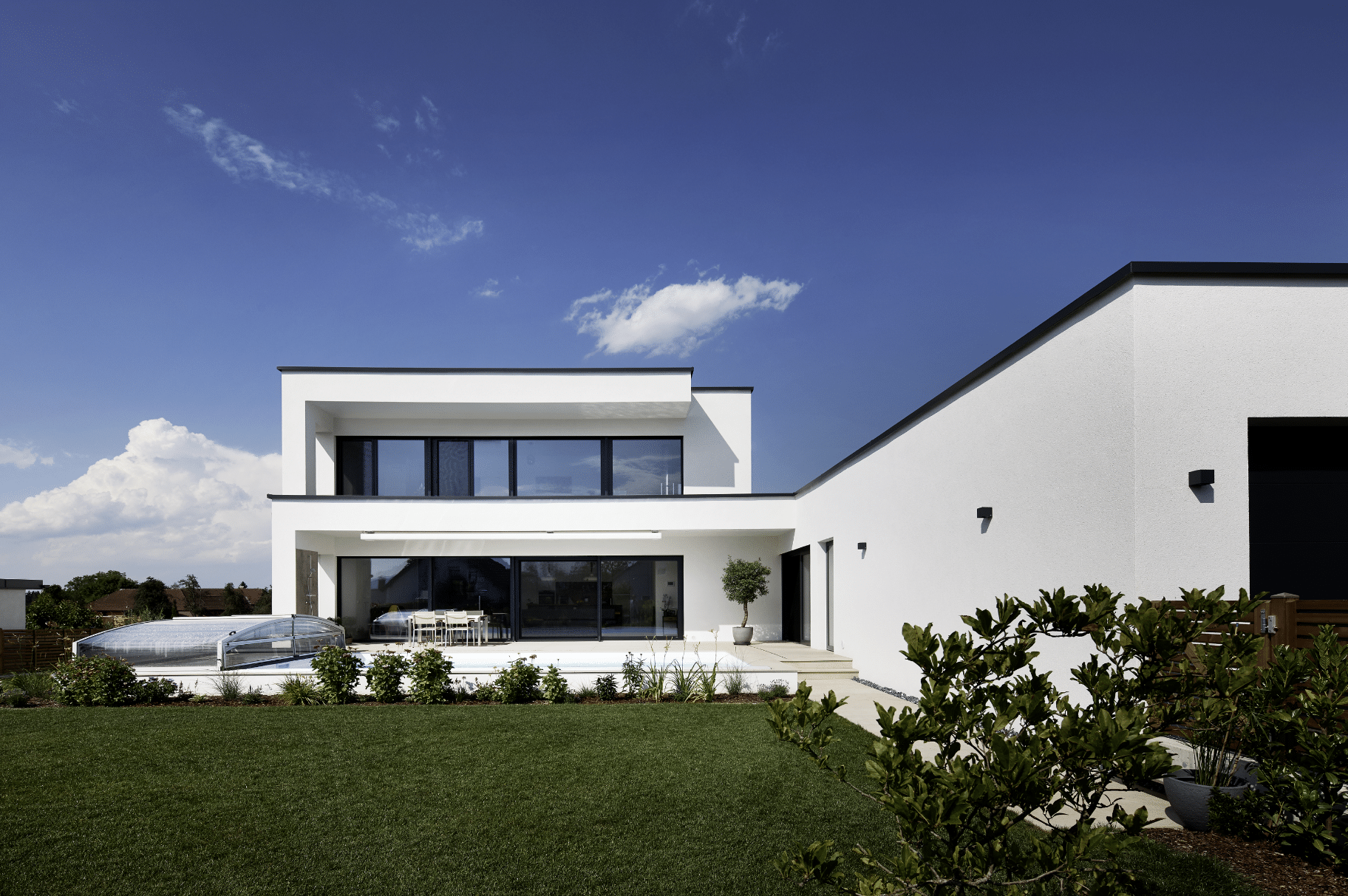 Neues Einfamilienhaus mit Flachdach, Terrasse mit Pool und Kunststoff-Alu-Fenstern und Hebeschiebetür aus der INLINE 91 SLIM von Gaulhofer.