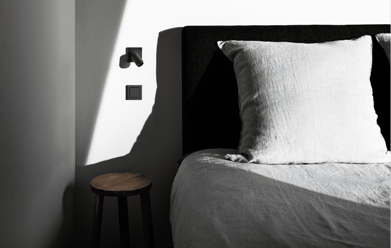 Gira zeigt ein Schlafzimmer mit praktischer Smart Home Lichtschalterlösung und in der Wand montierter Leuchte - beides in schwarz.