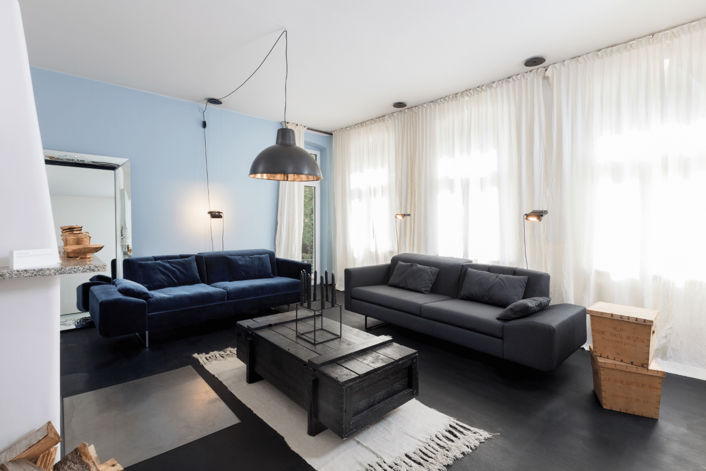Wohnzimmer mit Kamin, blauer Wand und dunkler Wohnlandschaft von Brühl erhältlich im Wohnhaus Grill & Ronacher.