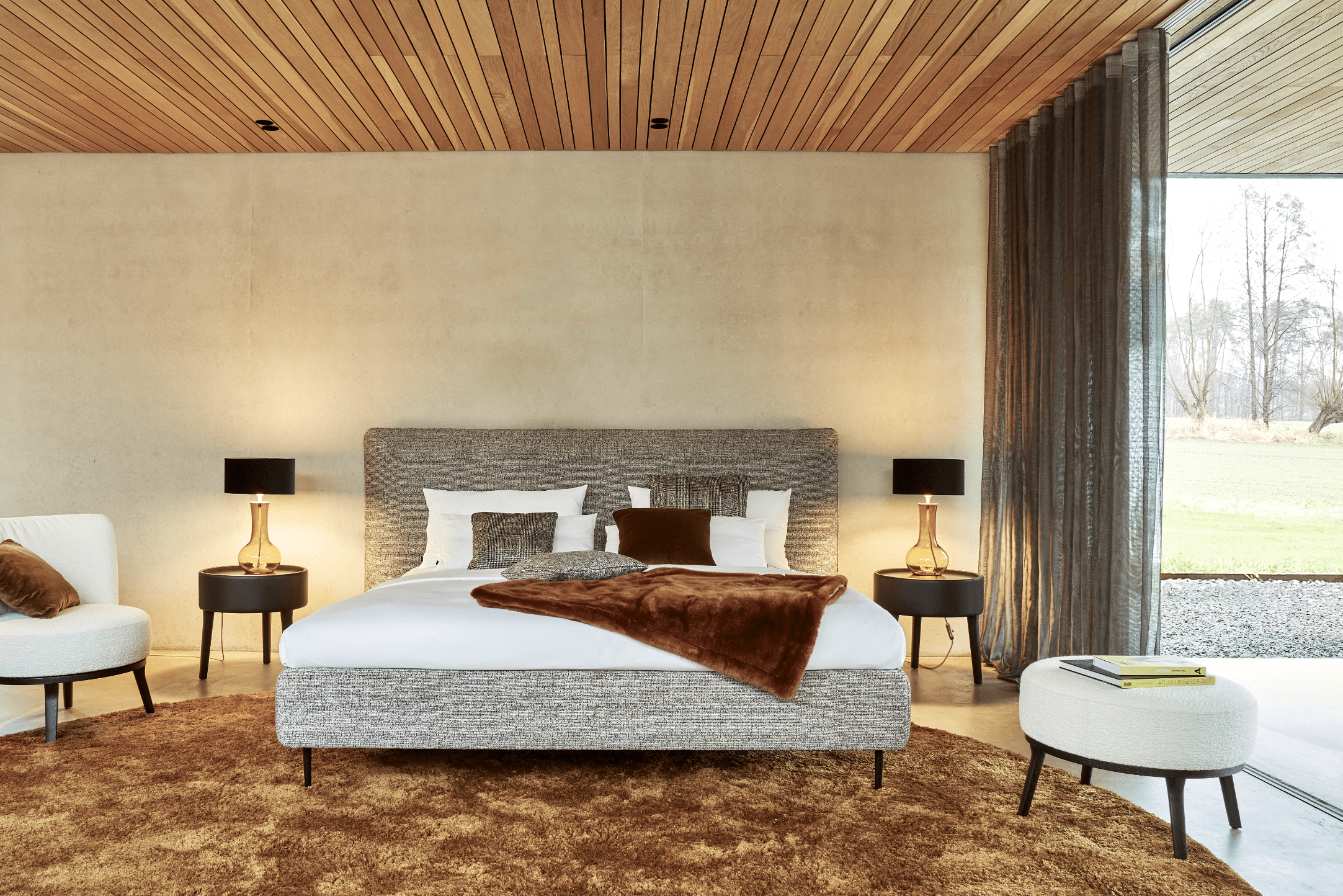 Grill & Ronacher zeigt ein modernes Schlafzimmer mit Doppelbett, schwarzen Lampen auf den Nachttischen und goldenem Rundteppich von Bielefelder Werkstätten.