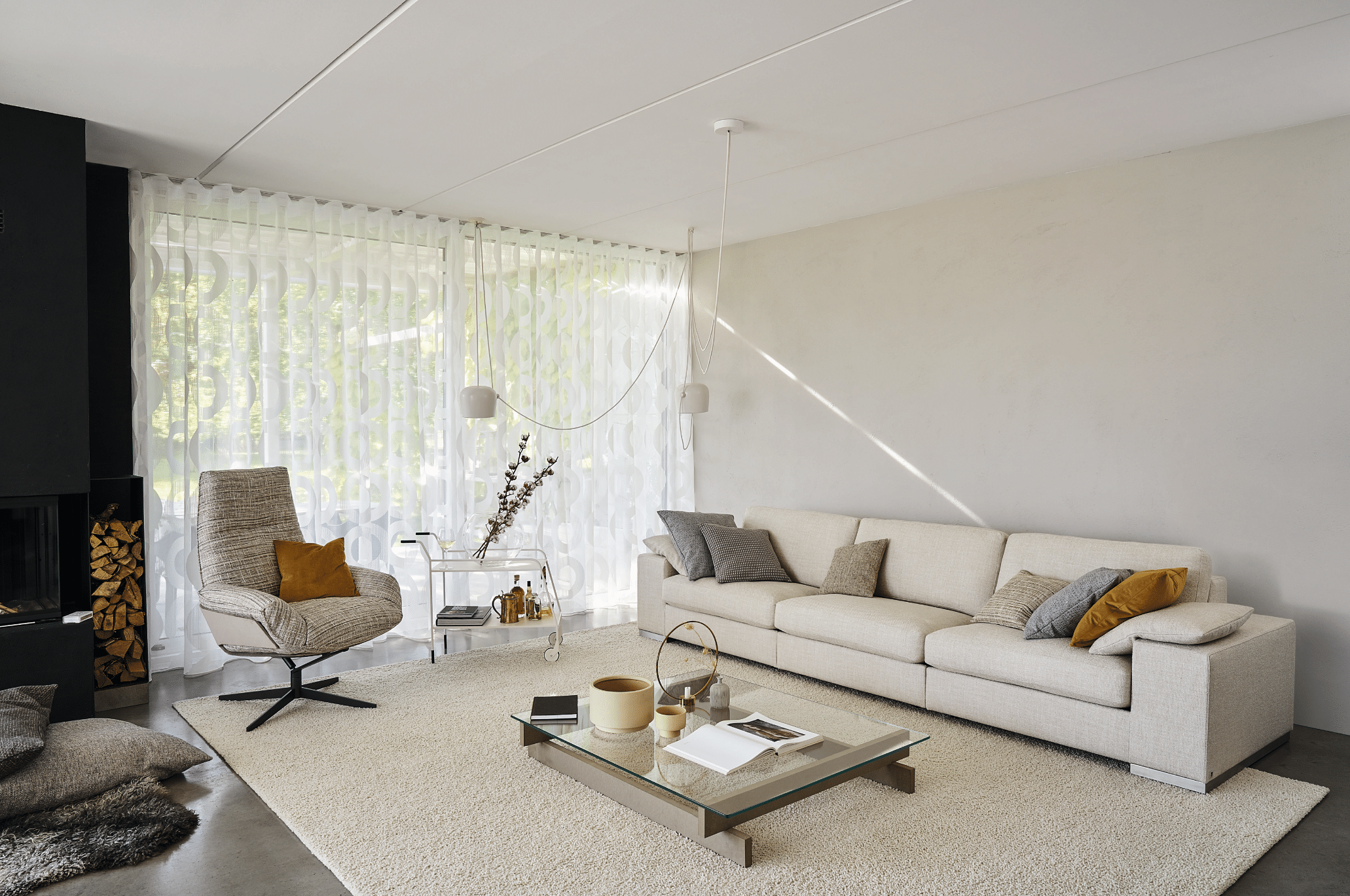 WOHNHAUS Grill & Ronacher zeigt ein Wohnzimmer mit einer langen, weissen Couch, einem freiliegendem Teppich in Naturweiss und einem gemütlichen Ohrensessel von Bielefelder Werkstätten.