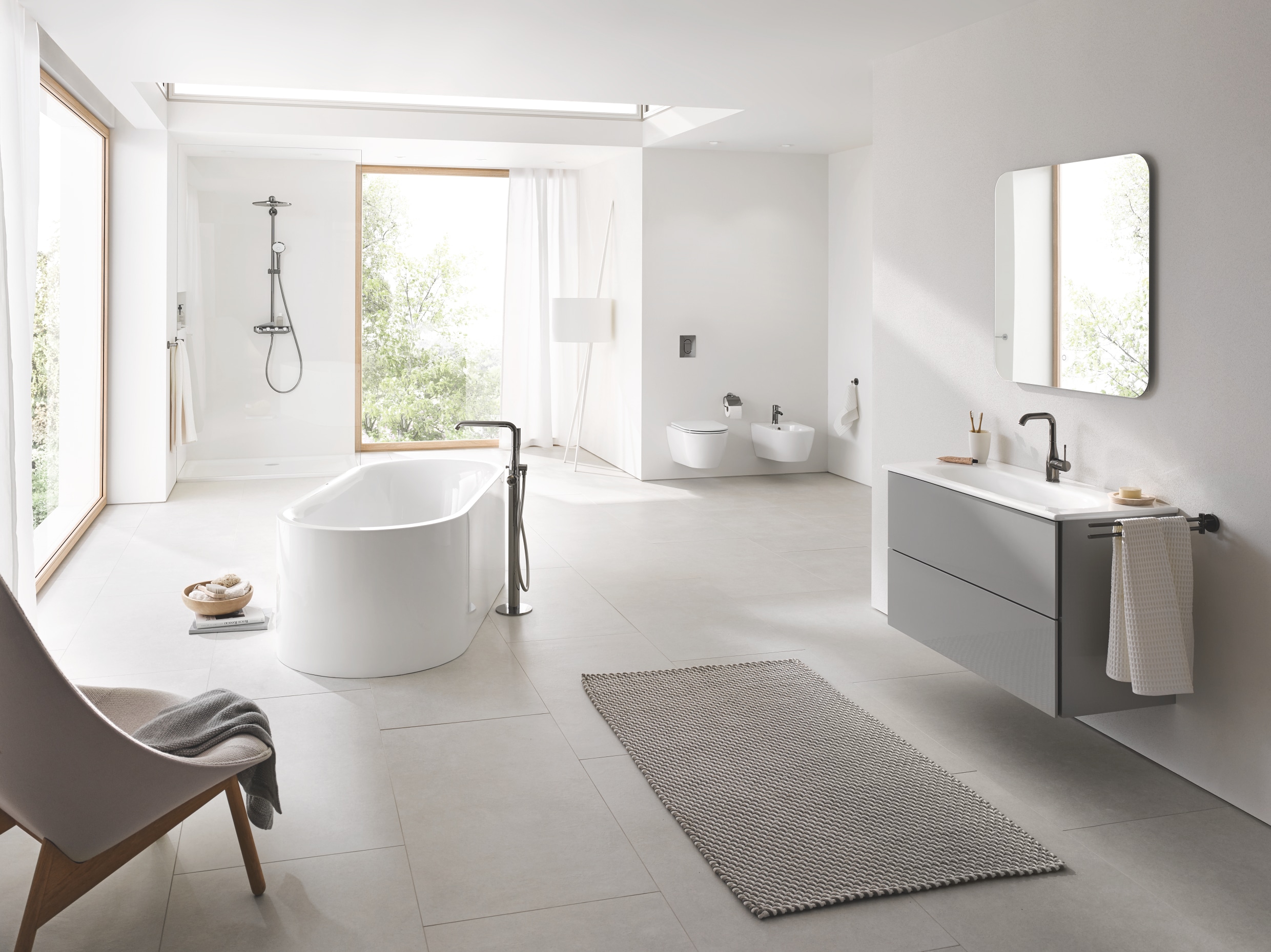 Badezimmer mit freistehender Wanne, einem Essence Keramik Waschtisch, dem Euphoria Smart Control Duschsystem, der Betätigungsplatte Arena Cosmopolitian und Essentials Accessoires von Grohe.