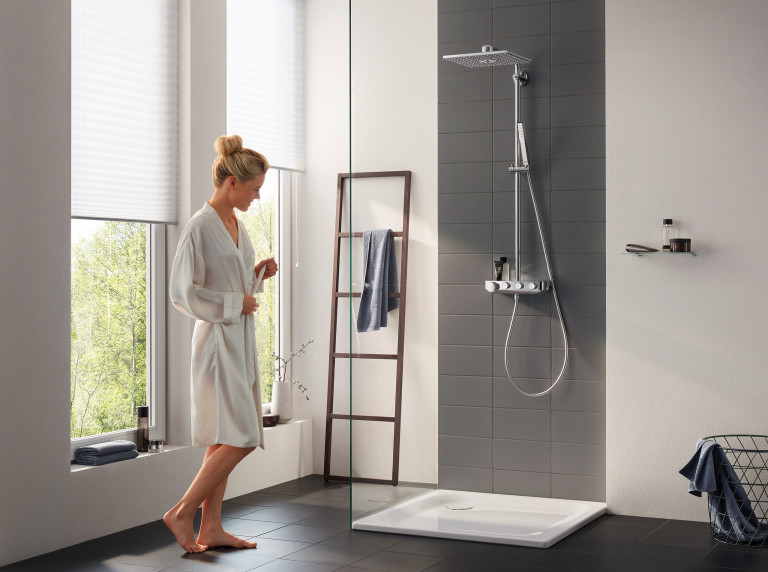 Duschnische mit eckiger Überkopf-Dusche und schmaler Hand-Dusche mit silber Chrom-Armaturen von Grohe mit dunklen Wandfliesen.