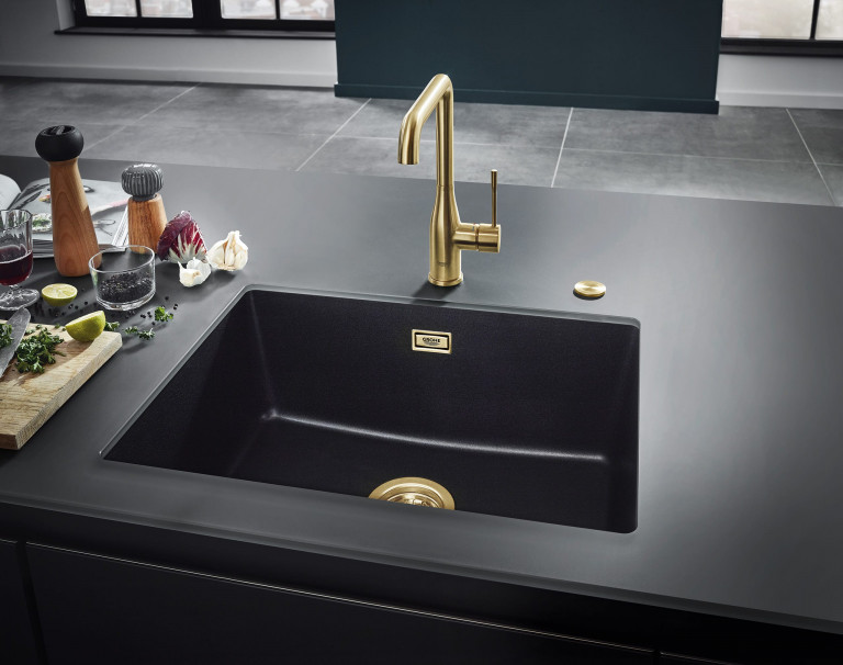 Schwarzes Spülbecken mit Armaturen aus gold von Grohe in schwarzer Arbeitsfälche.