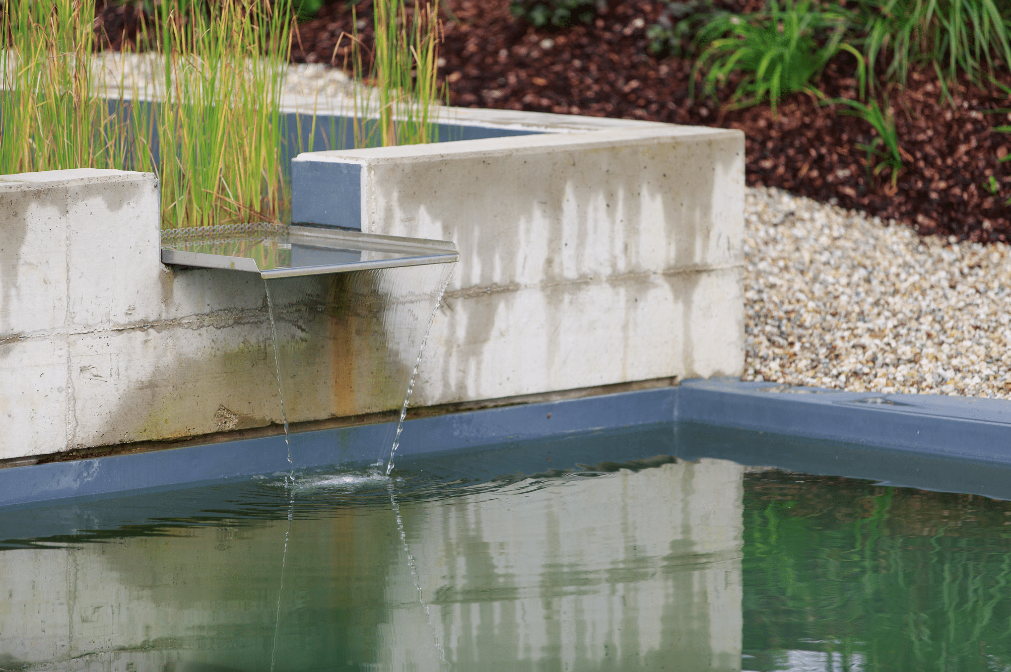 Hablesreiter zeigt einen kleinen Wasserfall der über ein Blech aus einer betonierten Mauer in den Pool hineinläuft.