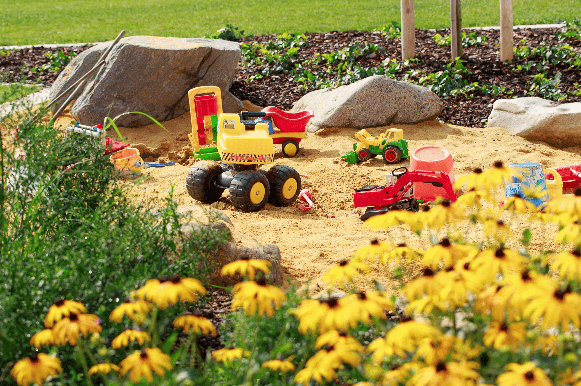 Hablesreiter zeigt eine Sandkiste mit gelben Blumen und mehreren Spielzeuge für Kinder.