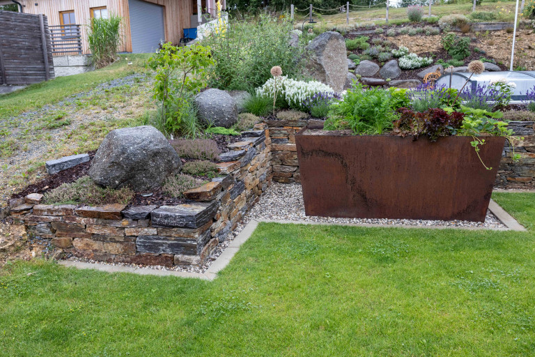 Beet mit Steinmauer, großer Blumentopf aus Eisen in rostiger Optik und Rasenfläche von Gartengestaltung Hablesreiter.