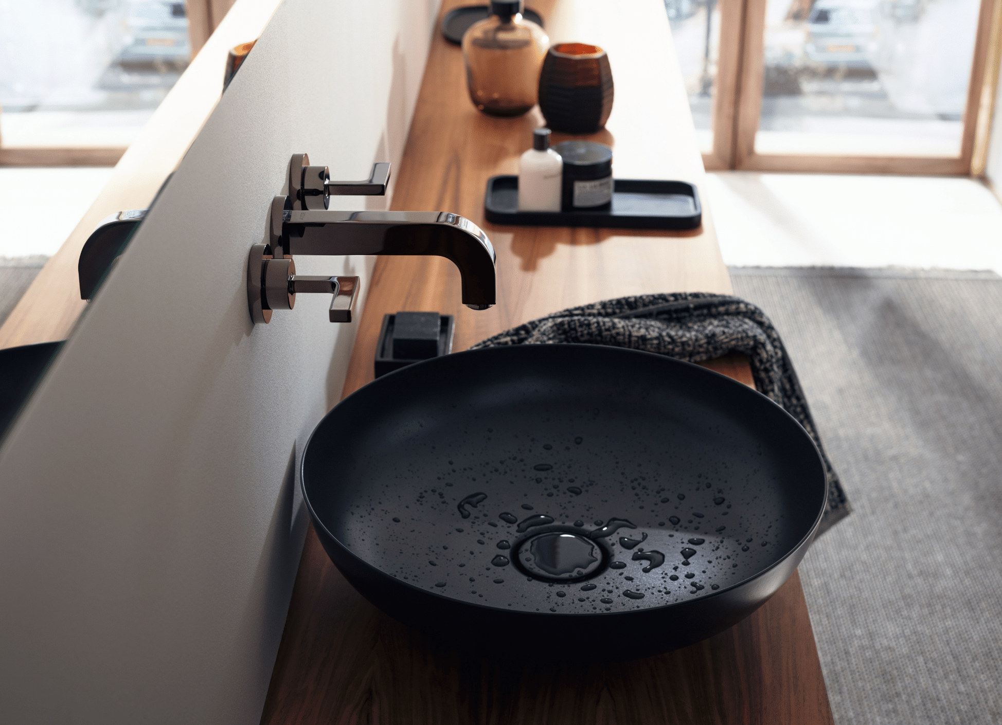 Hansgrohe zeigt eine runde, schwarze Waschschüssel mit glänzend brauner Armatur auf einem Waschtisch in Holzoptik.